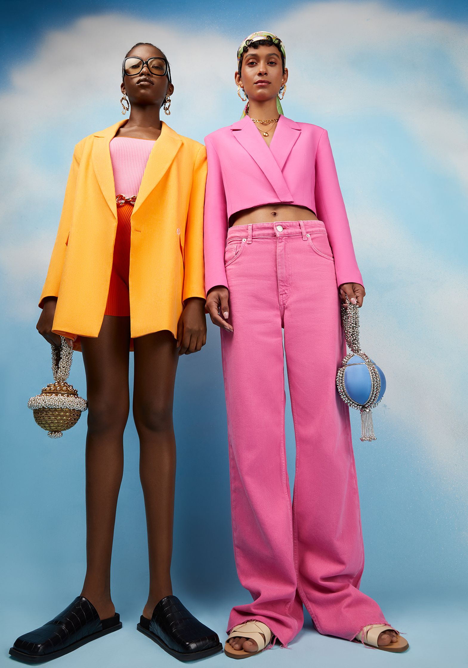two women in pink pants and blazers are posing in front of a blue sky