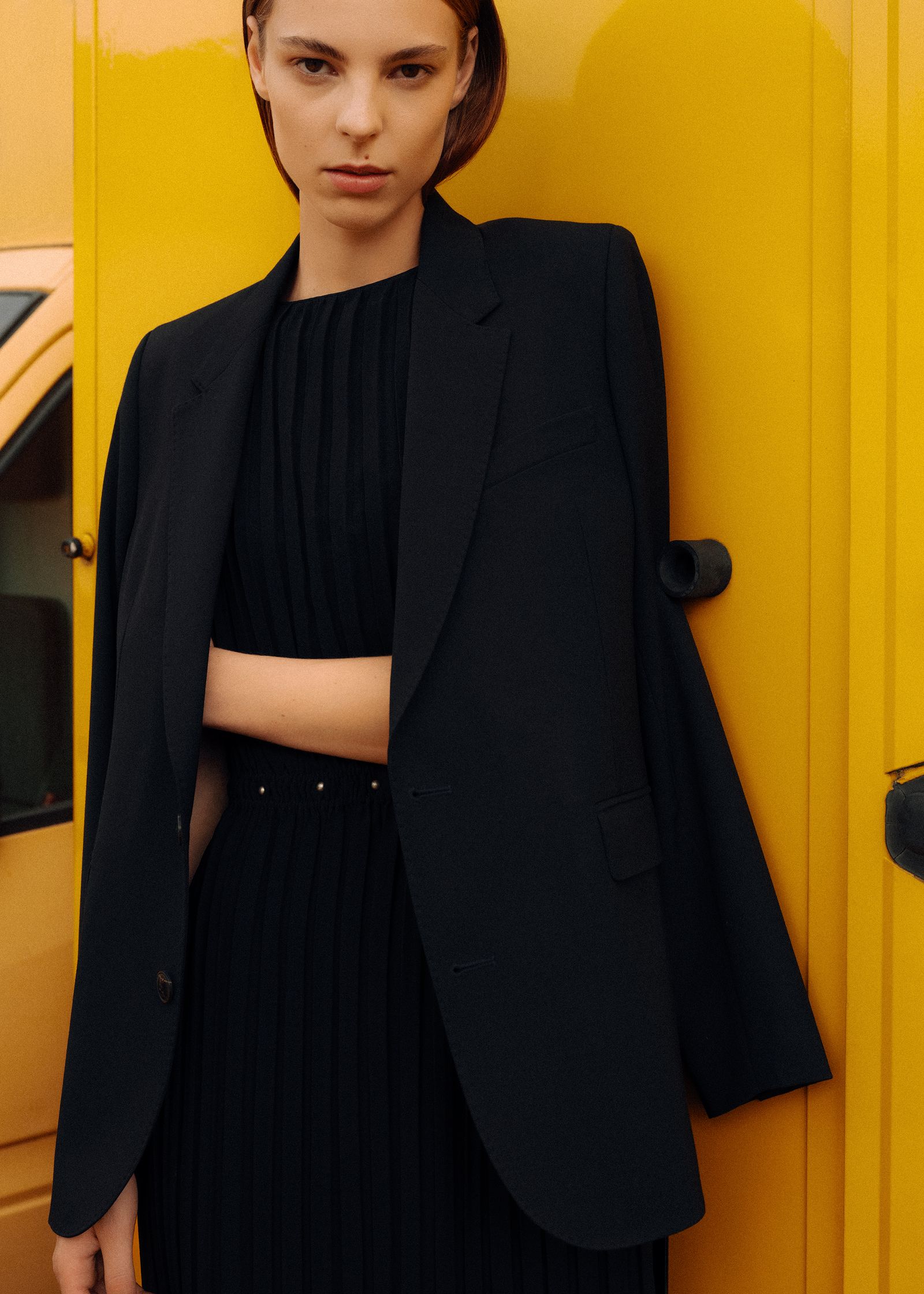 a woman in a black blazer leaning against a yellow van