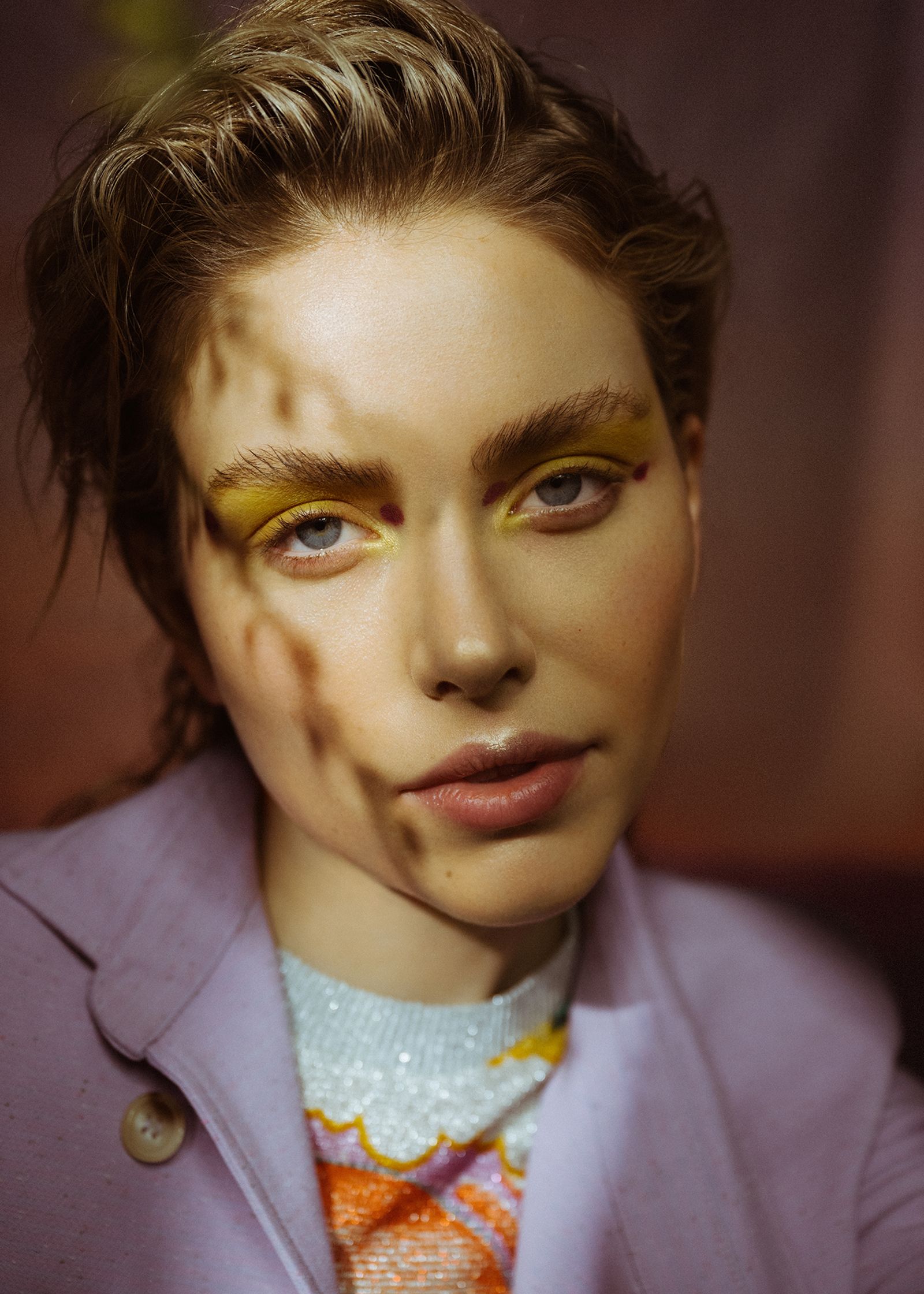 a woman wearing a purple jacket and yellow eye makeup