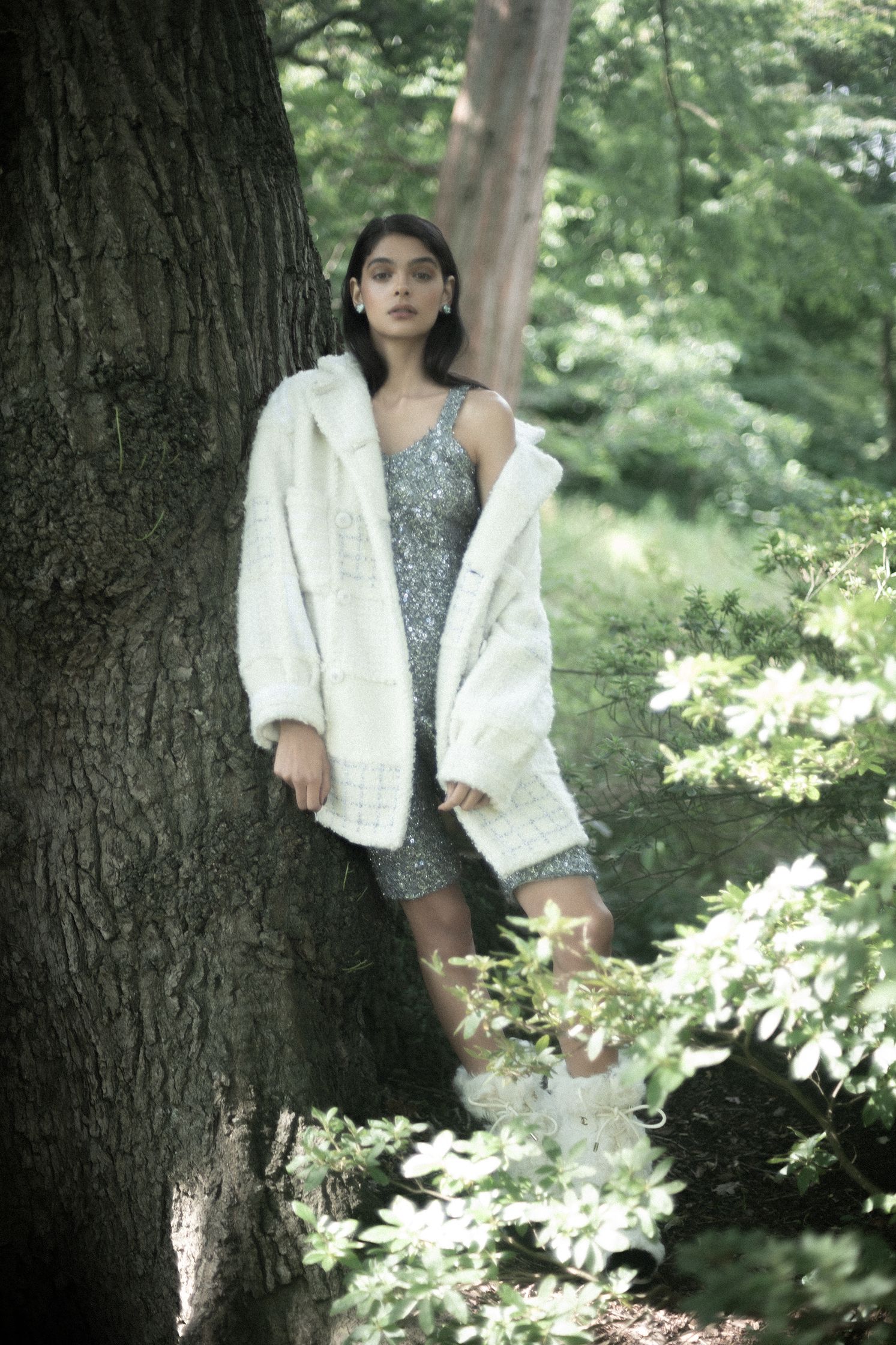 a woman in a white fur coat leaning against a tree