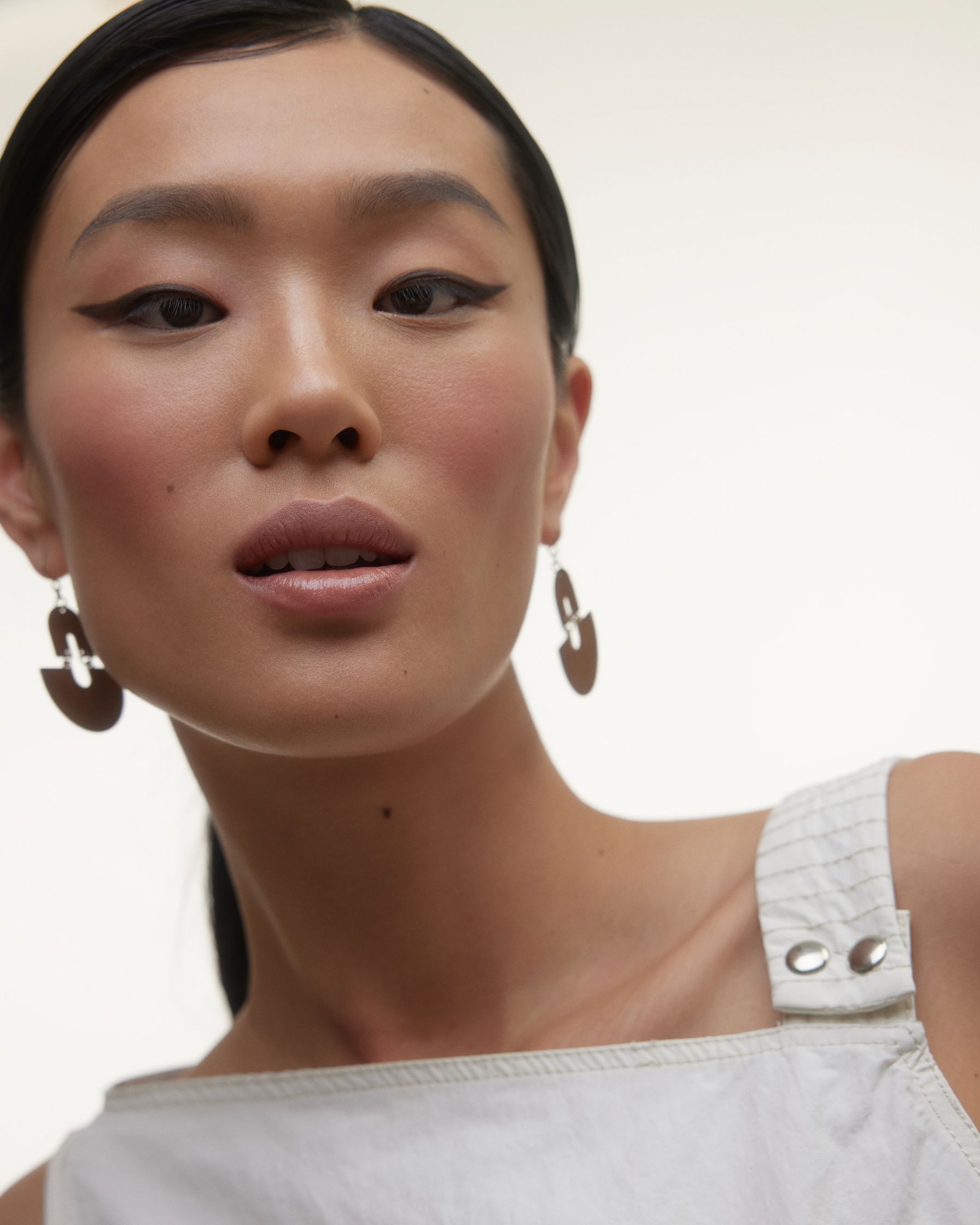 a model wearing white overalls and a pair of brown earrings