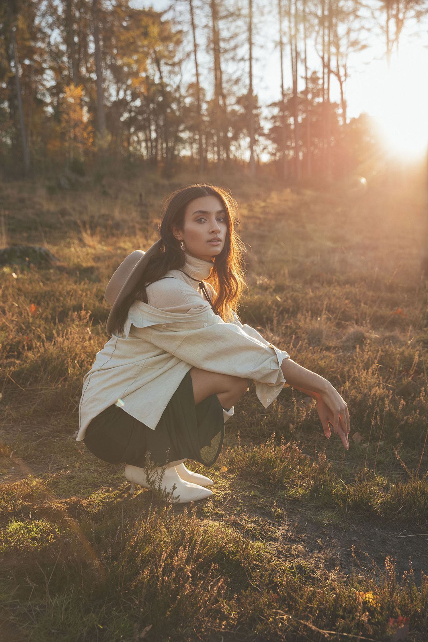 a woman crouching in a field at sunset