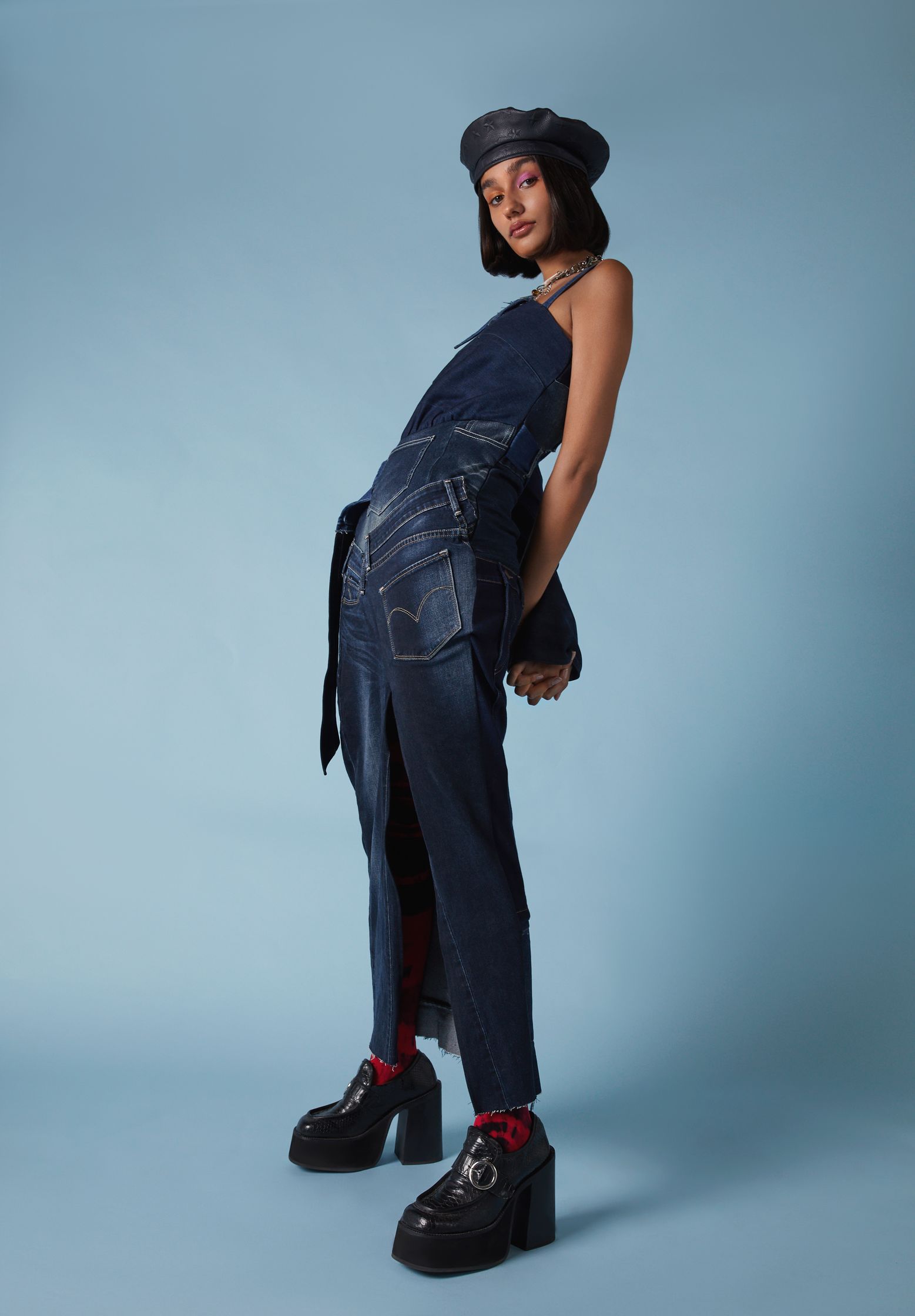 a woman in denim overalls posing on a blue background