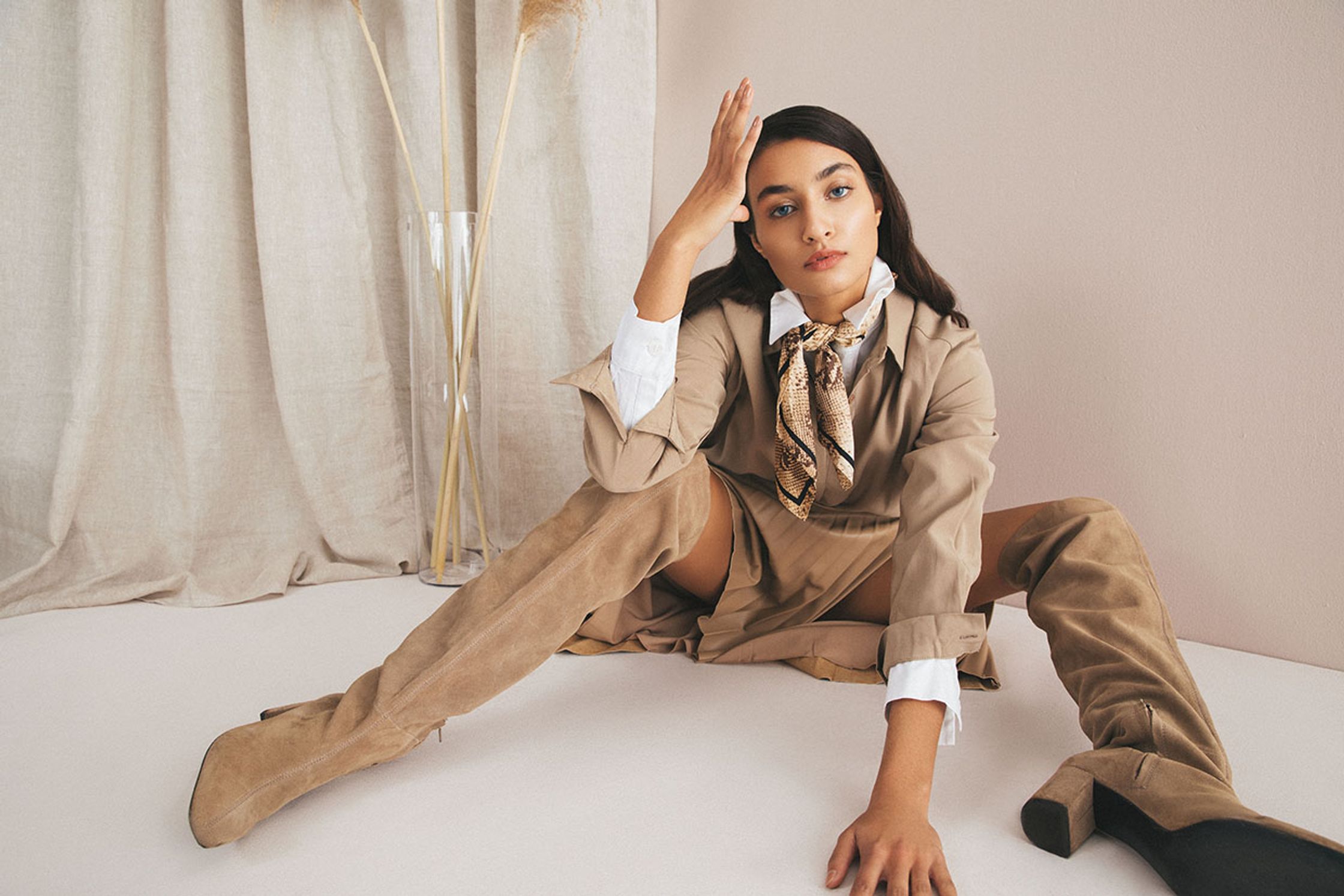 a woman sitting on the floor in a tan coat and thigh high boots