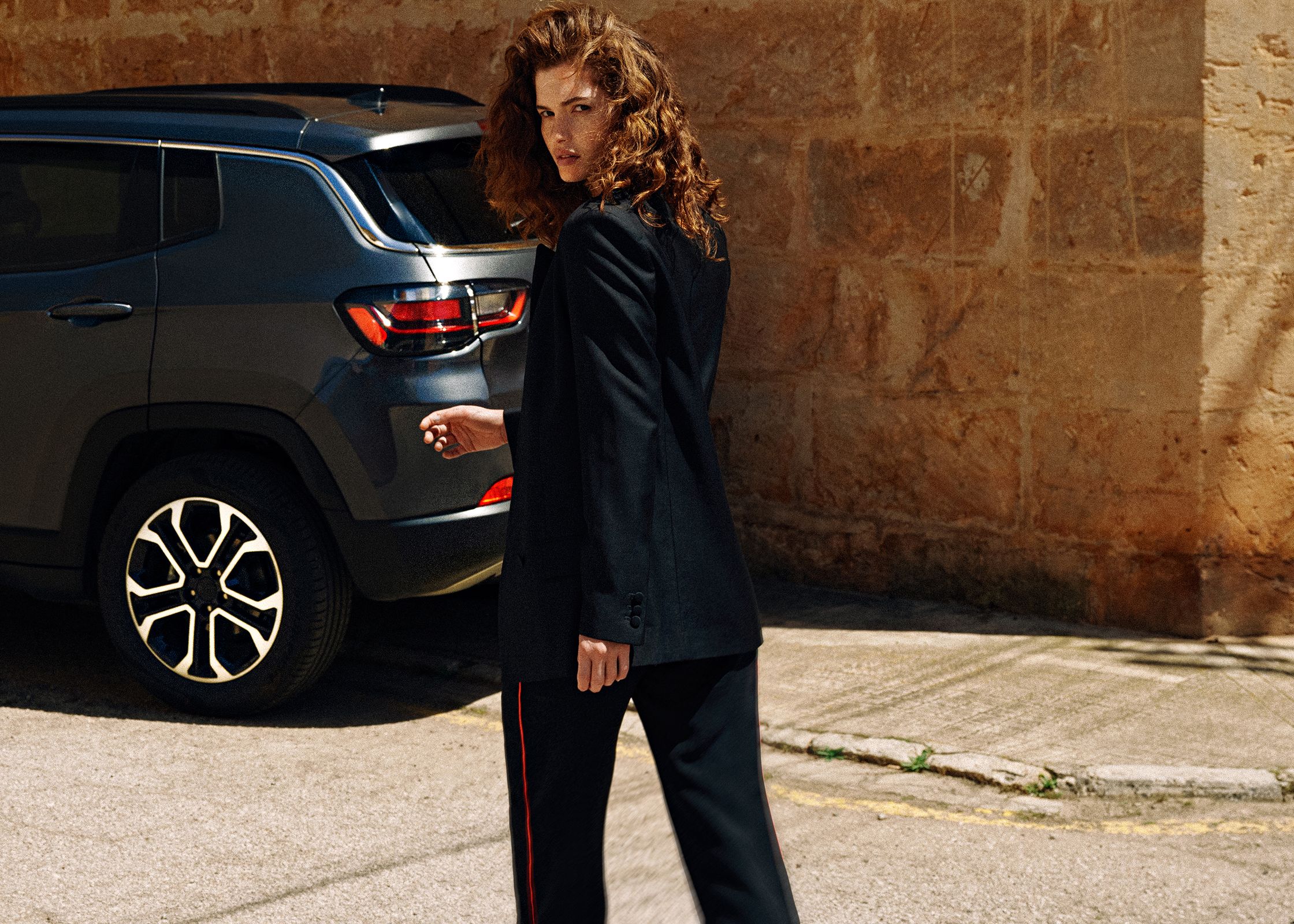 a woman in a suit is standing next to a jeep compass