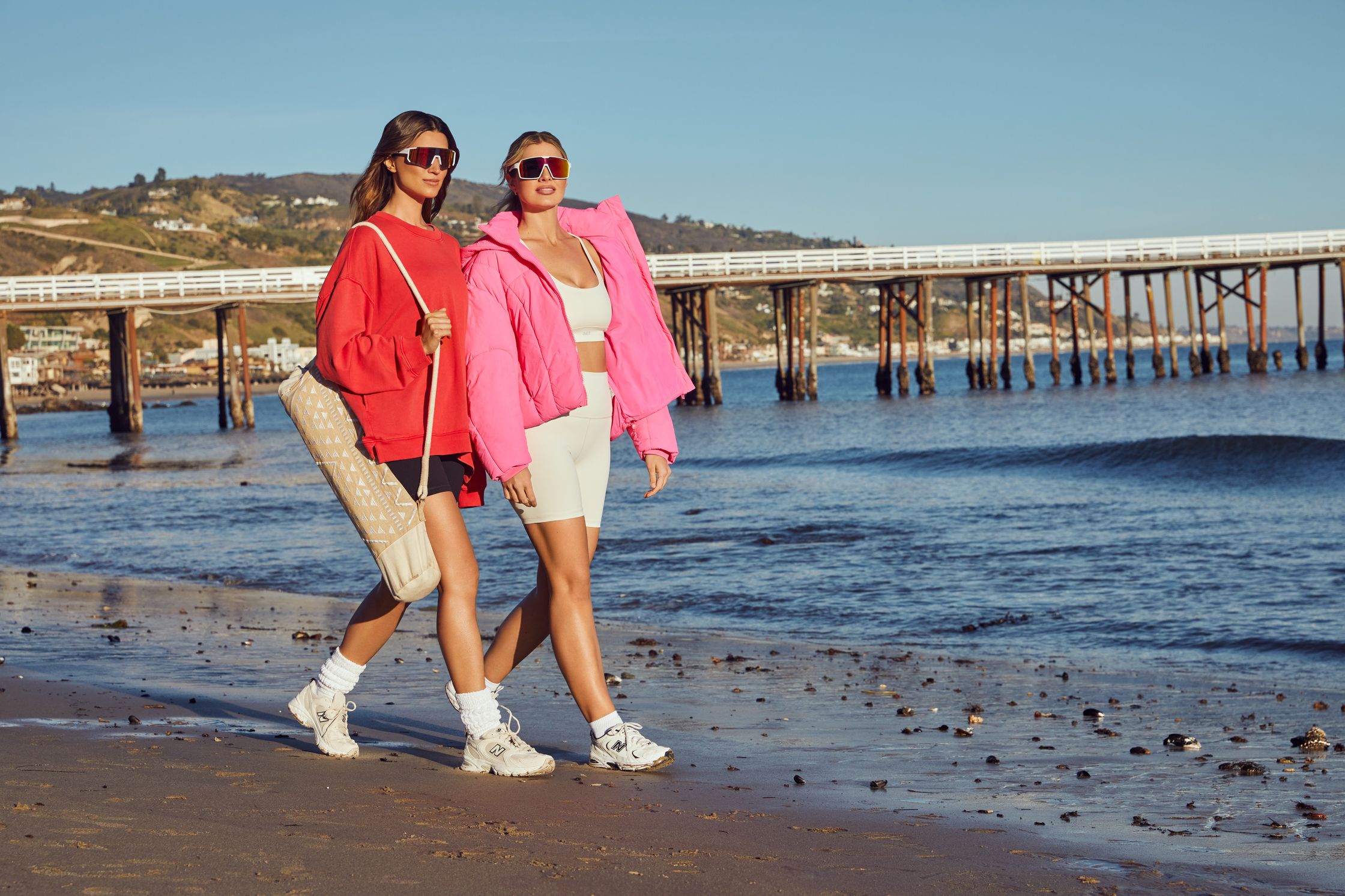 two women walking on the beach near a pier