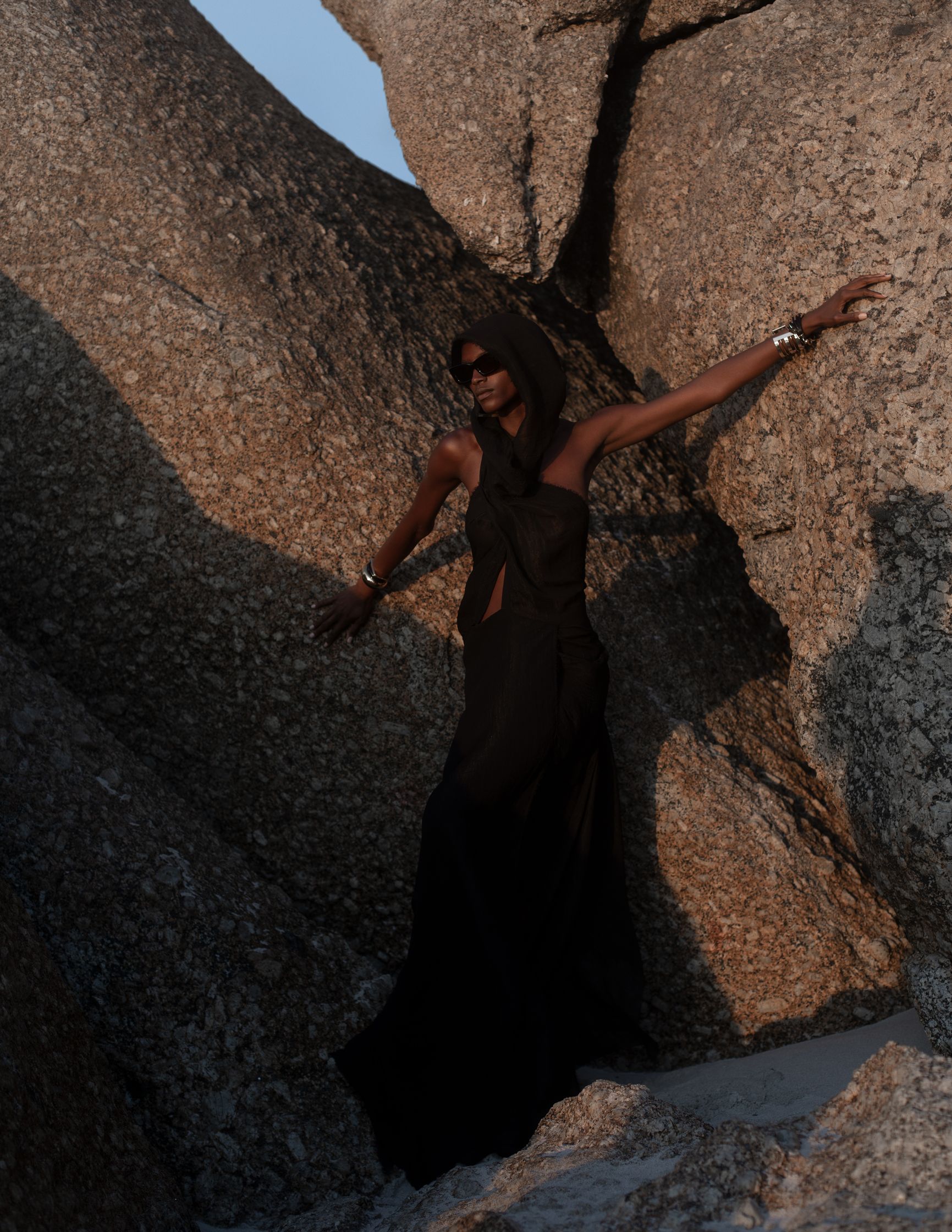 a woman in a black dress standing on a large rock