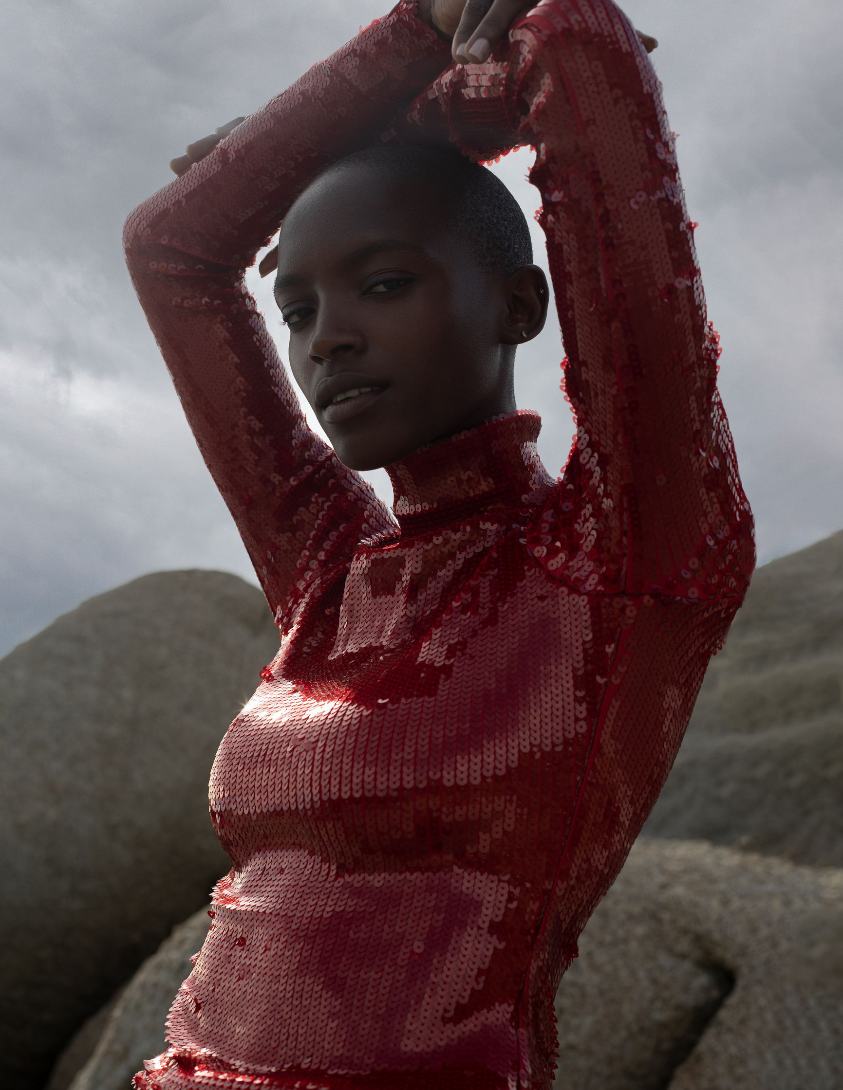 a black woman in a red sequined top posing on rocks