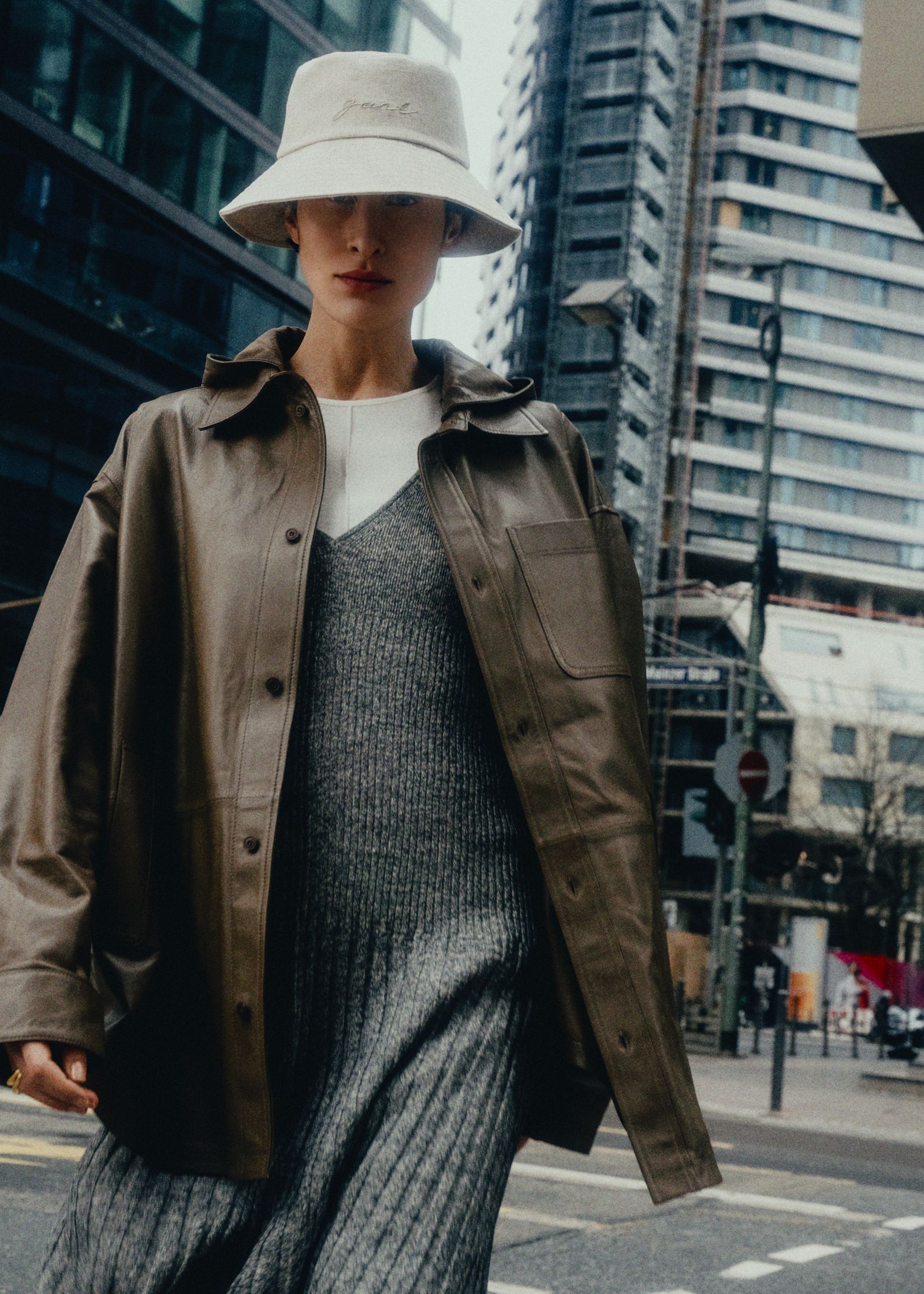 a woman wearing a hat and a leather jacket on a city street