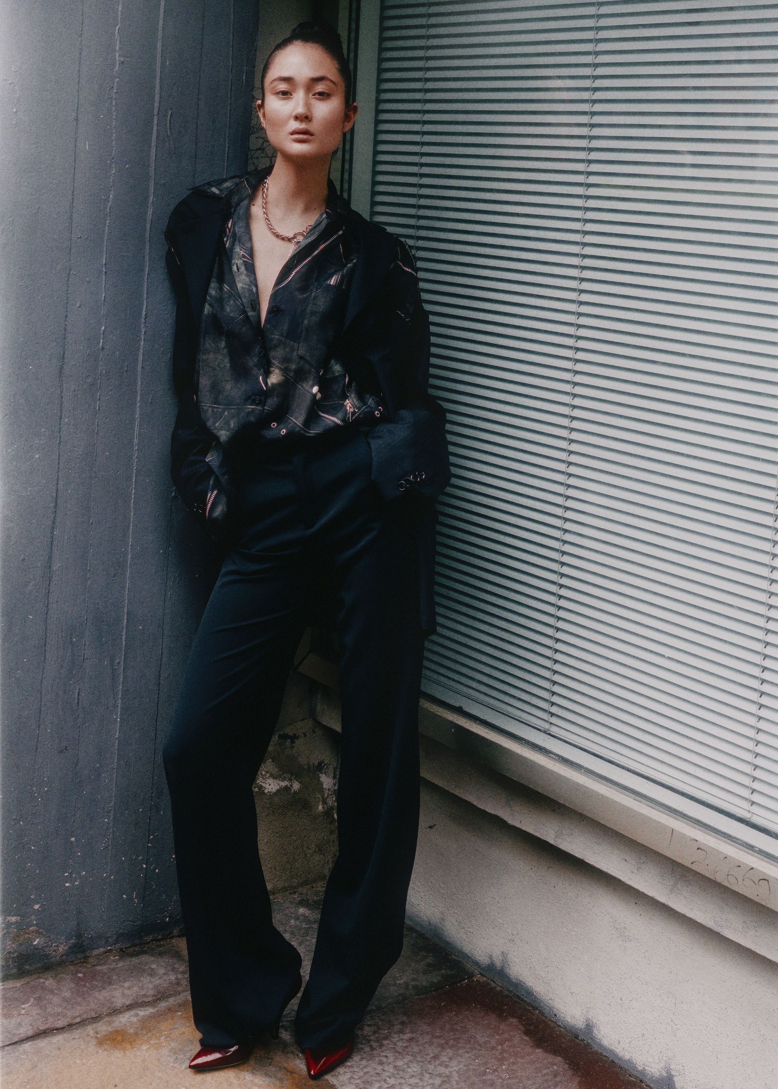 a woman in black pants leaning against a wall