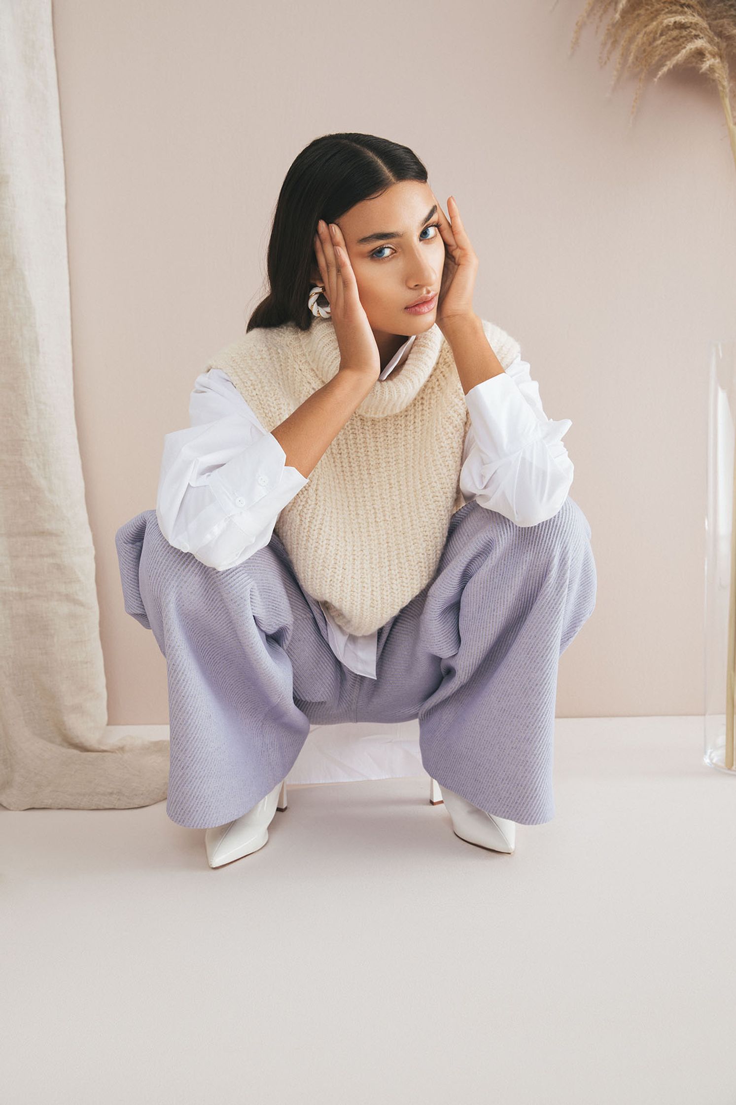 a woman in a white sweater and purple pants crouching on the floor