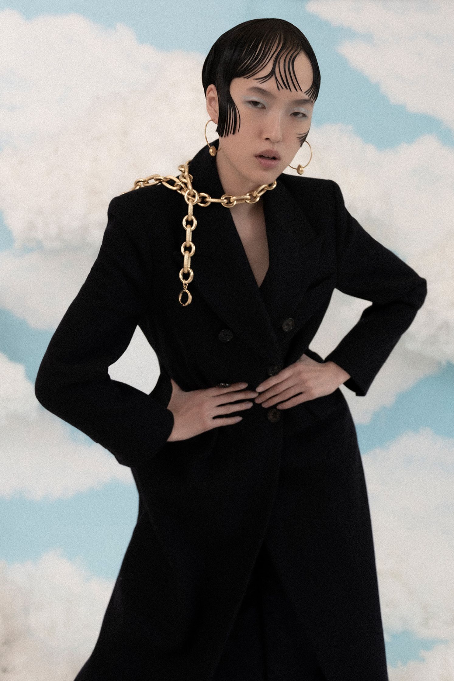 a model wearing a black coat and chain necklace