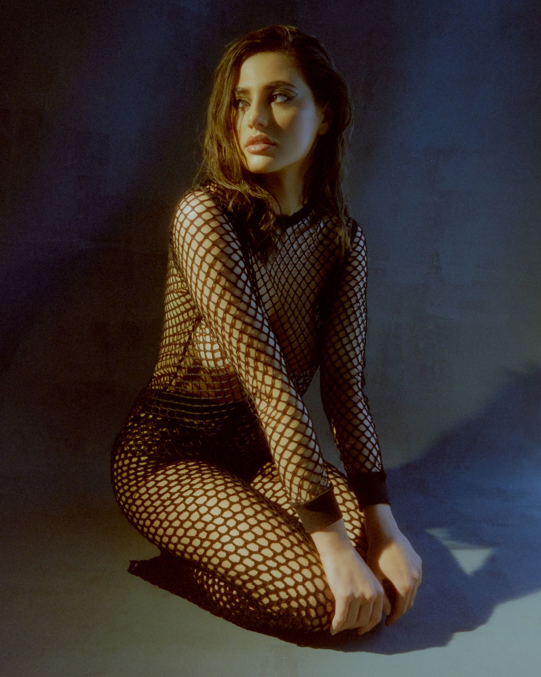 a woman in a fishnet bodysuit sitting on the ground
