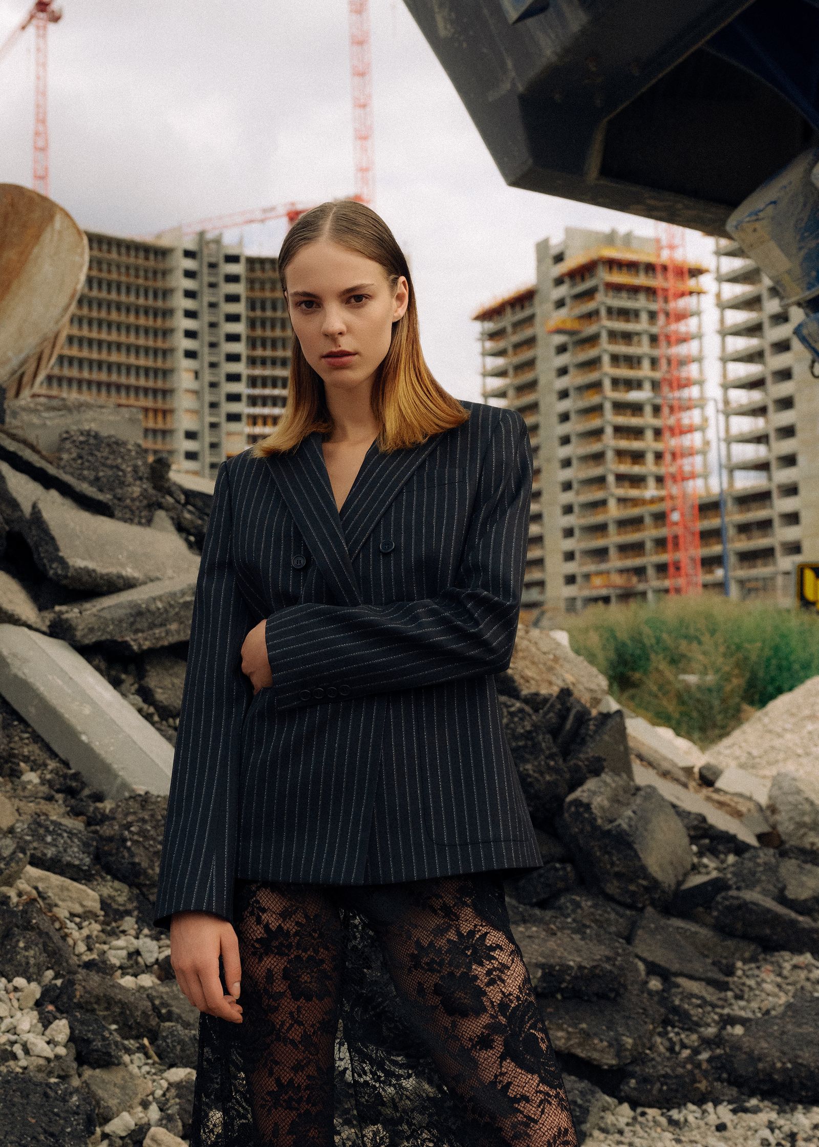 a woman in a black blazer standing in front of a pile of rubble