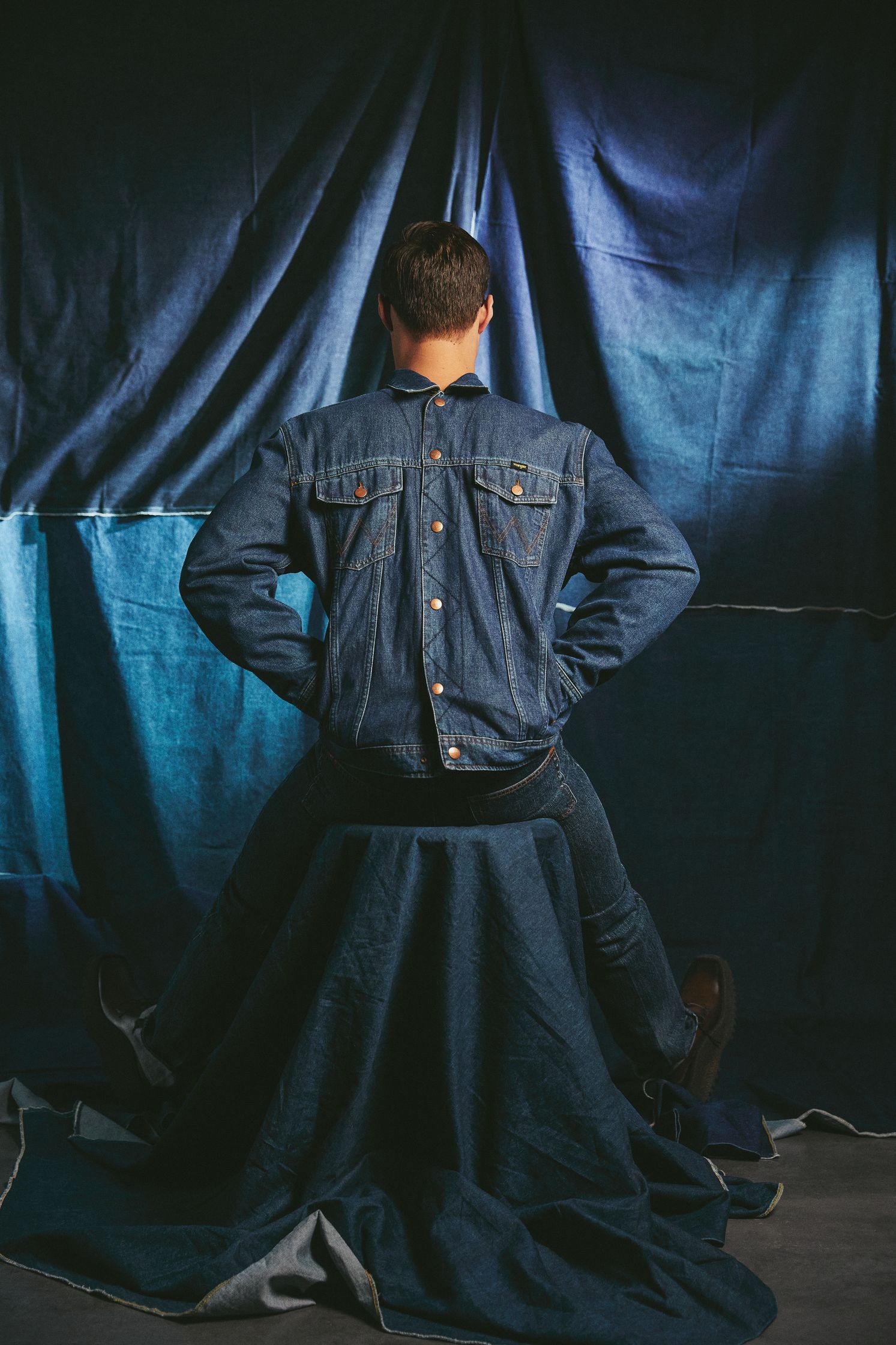 a man in a denim jacket sitting on a blue cloth