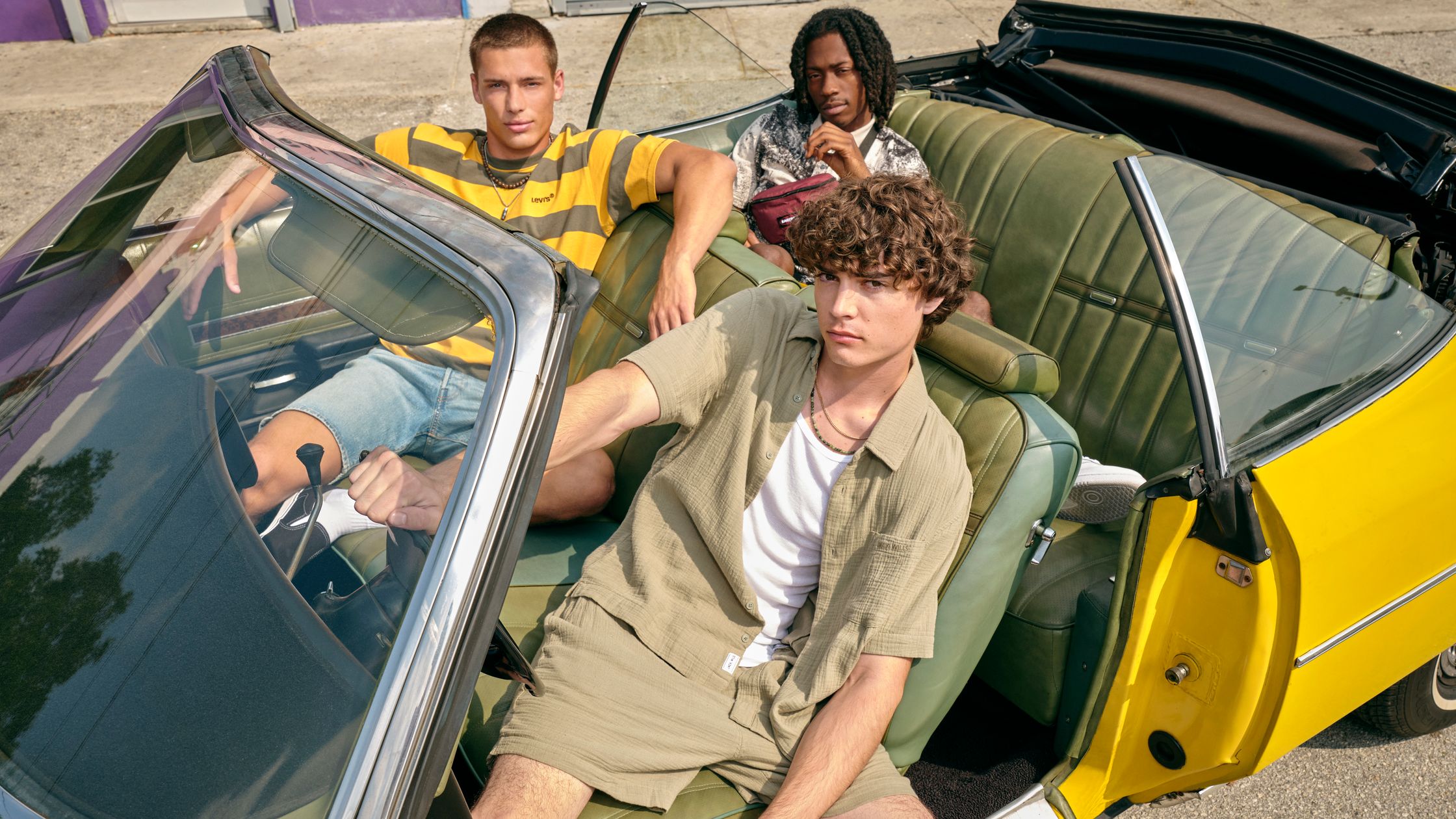 three young men sitting in the back of a yellow convertible car