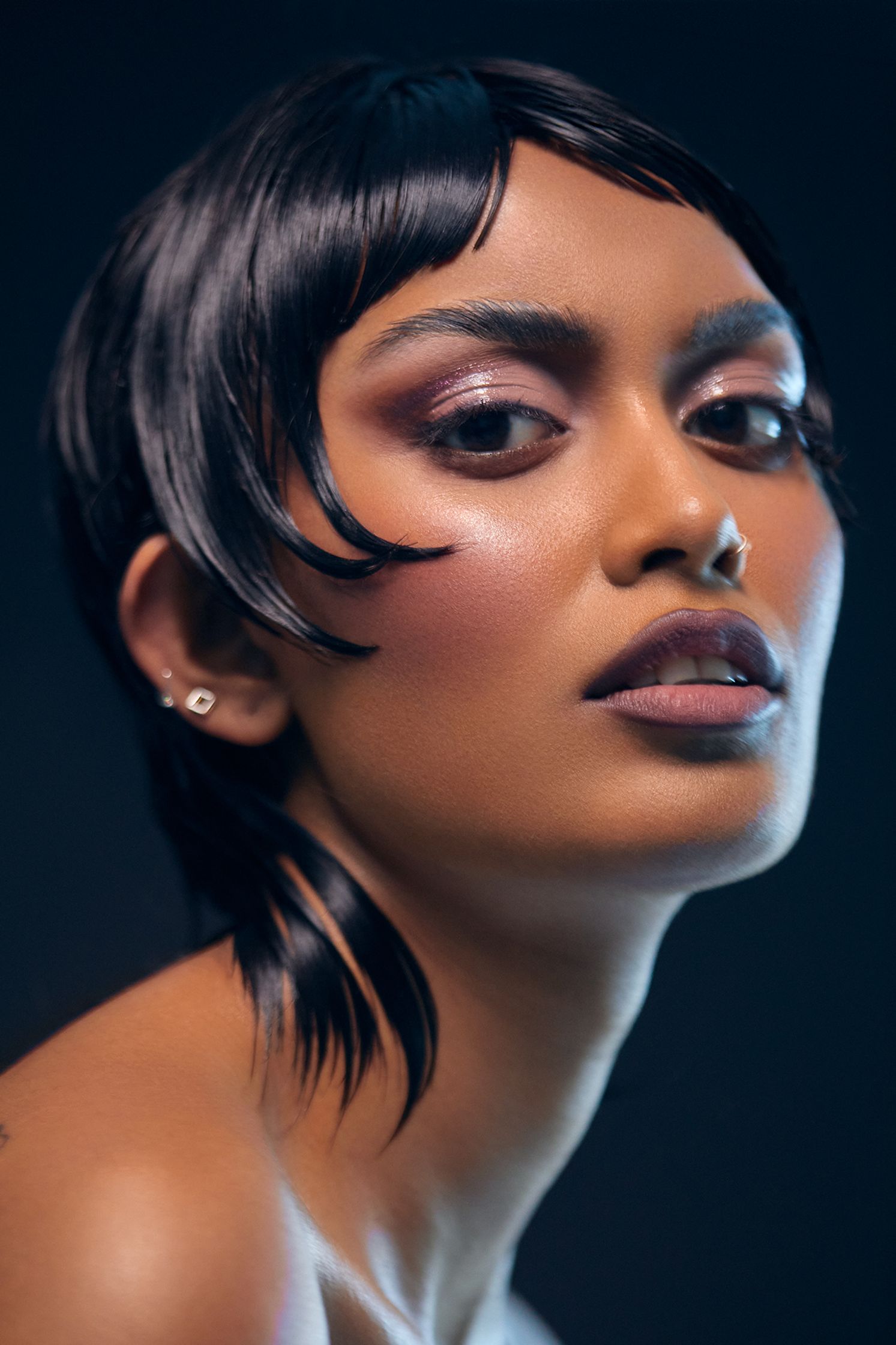 a beautiful woman with black hair and tattoos posing on a dark background