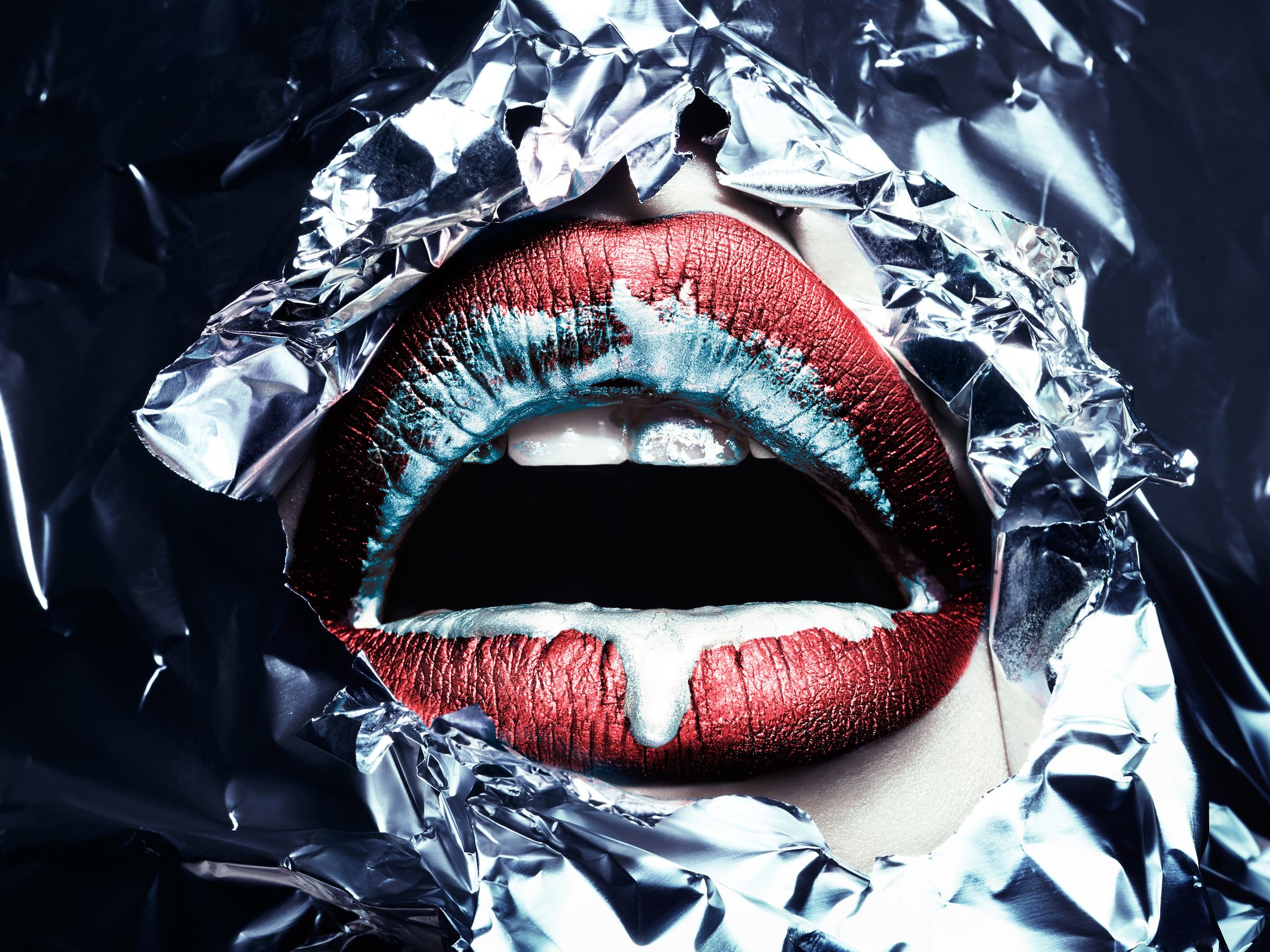 Close-up of lips painted in metallic red and blue hues, framed by crumpled aluminum foil, symbolizing the suffocating effects of pollution and waste.