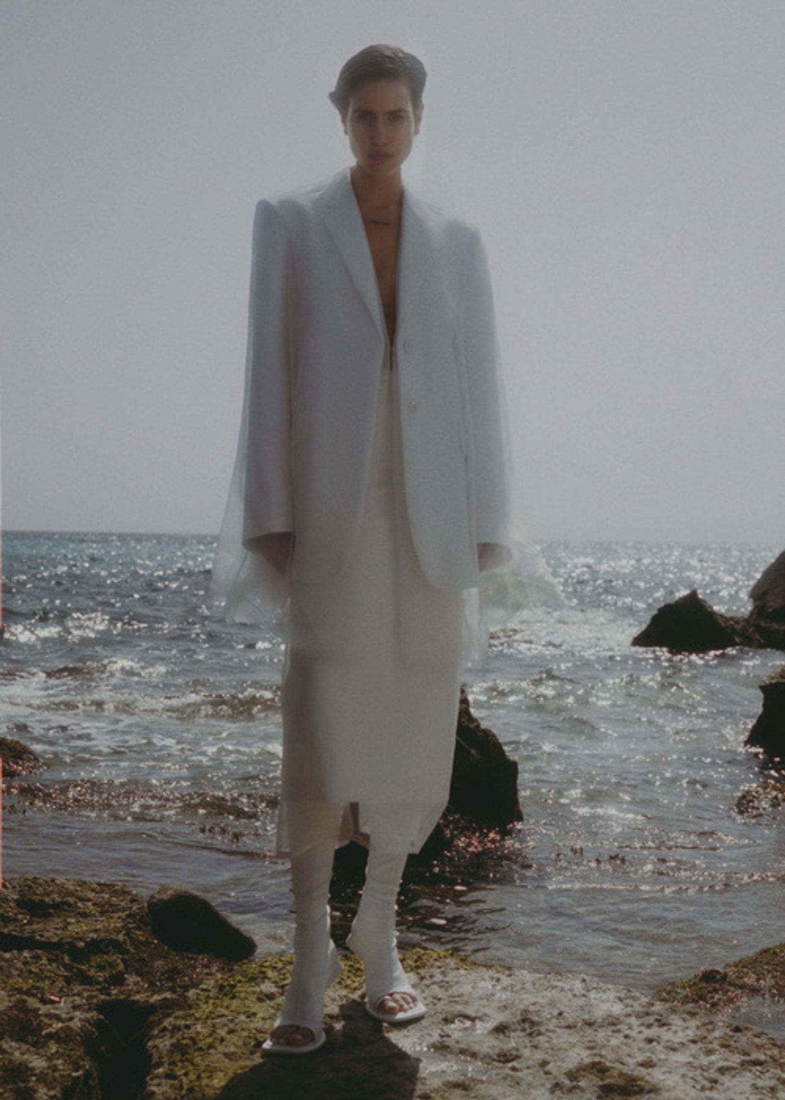 a man in a white suit standing on rocks near the ocean