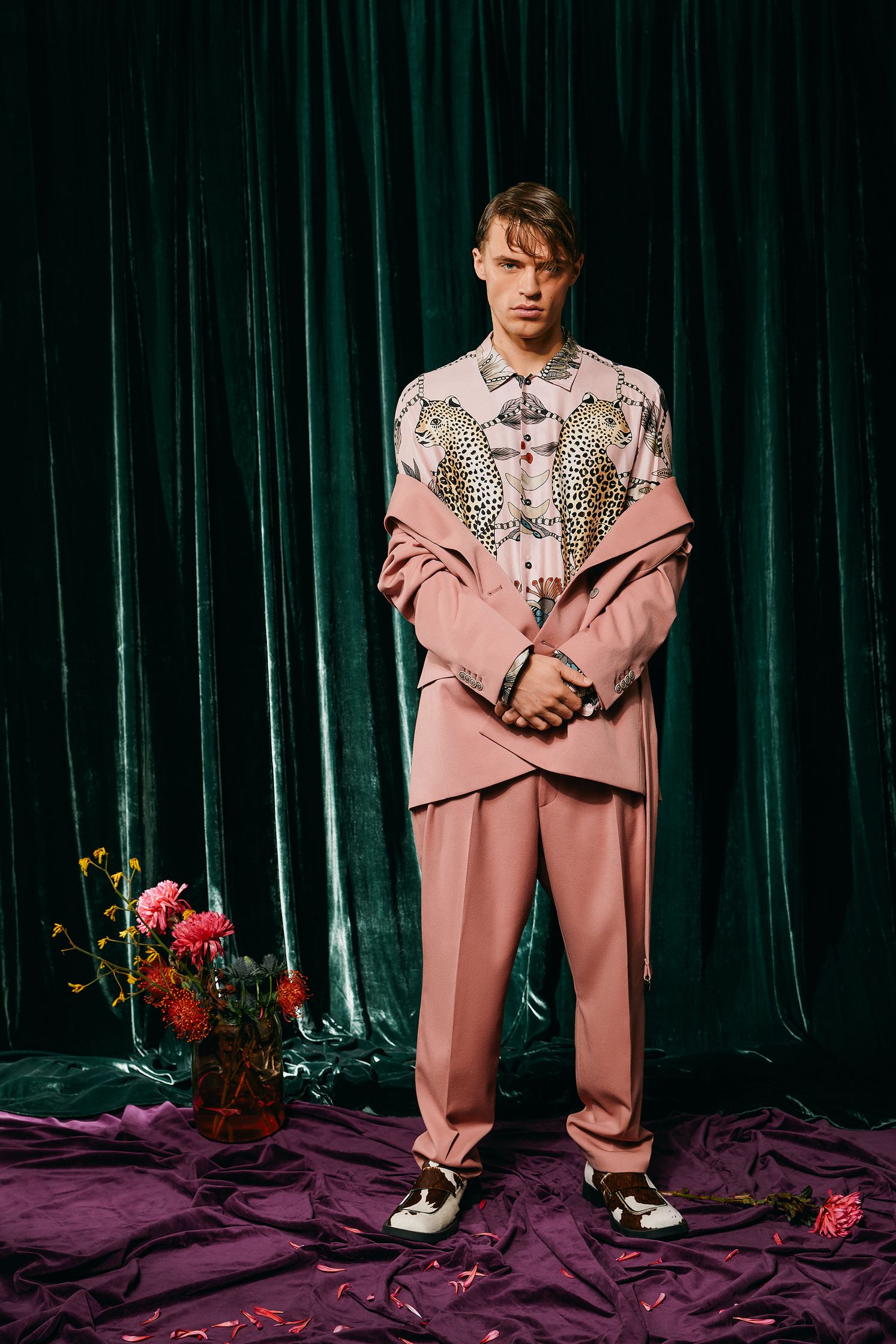 a man in a pink suit standing in front of a purple curtain