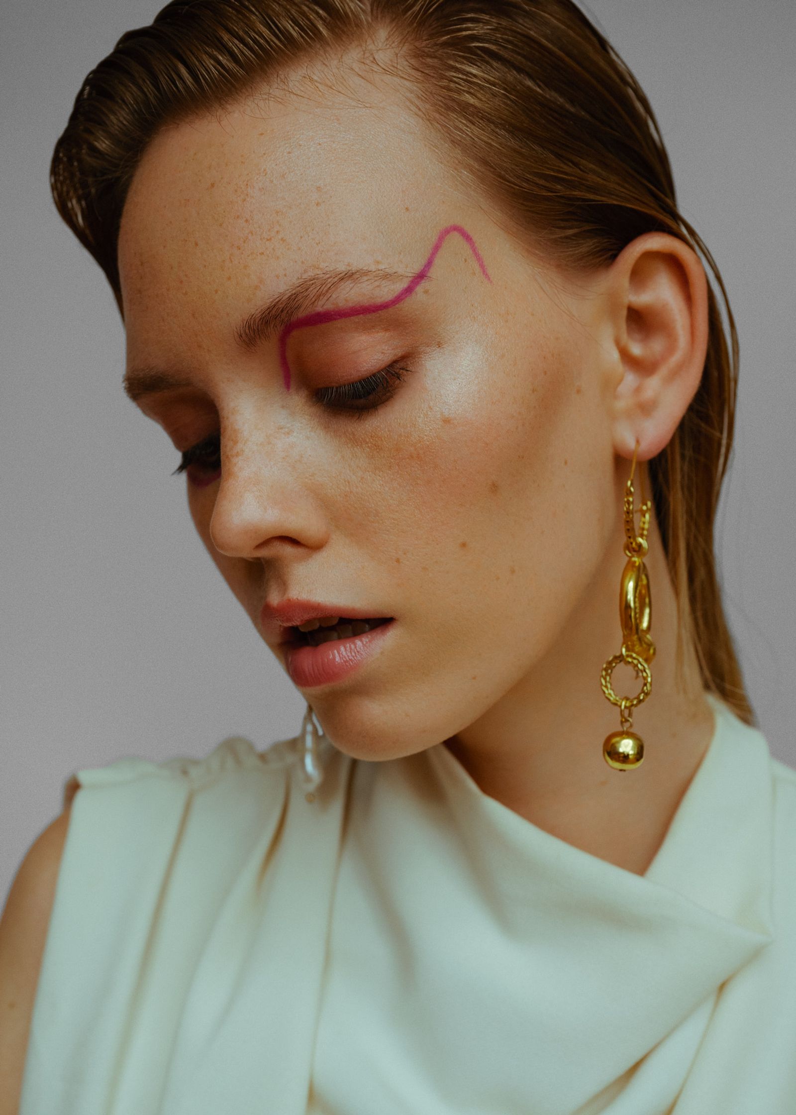 a woman wearing gold earrings with a pink eye