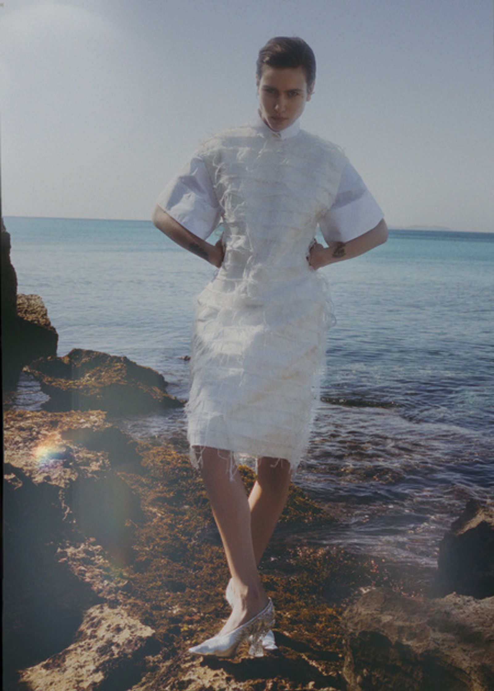 a woman in a white dress standing on rocks near the ocean
