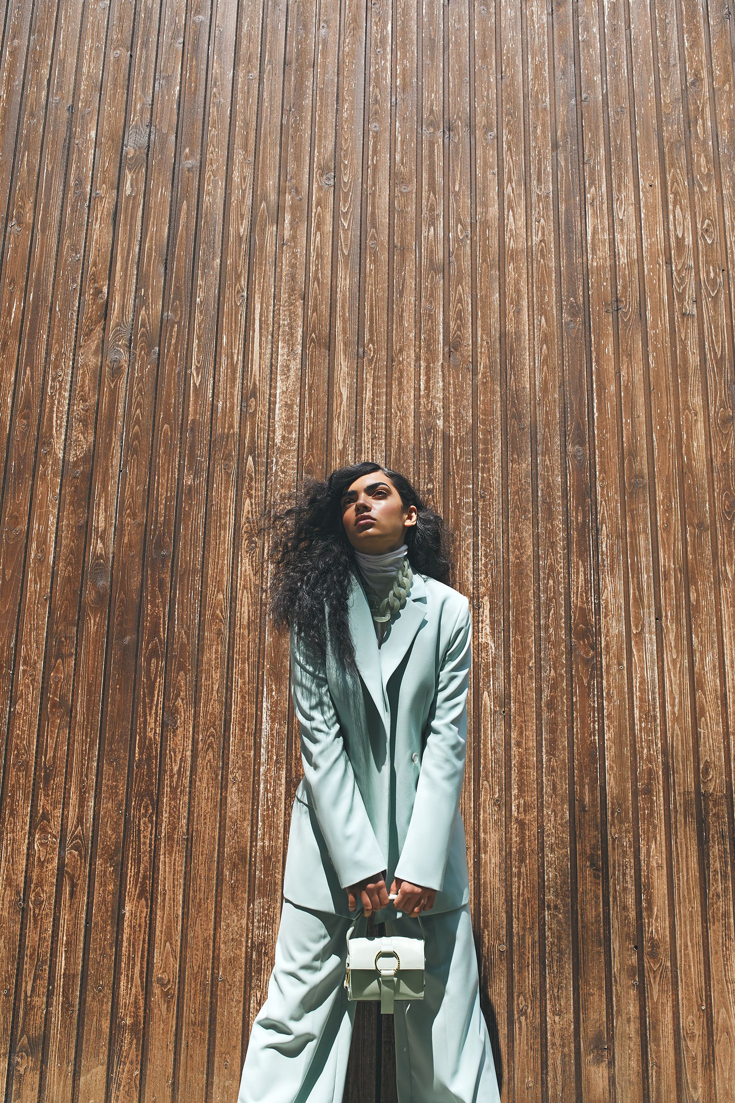 a woman in a suit leaning against a wooden wall