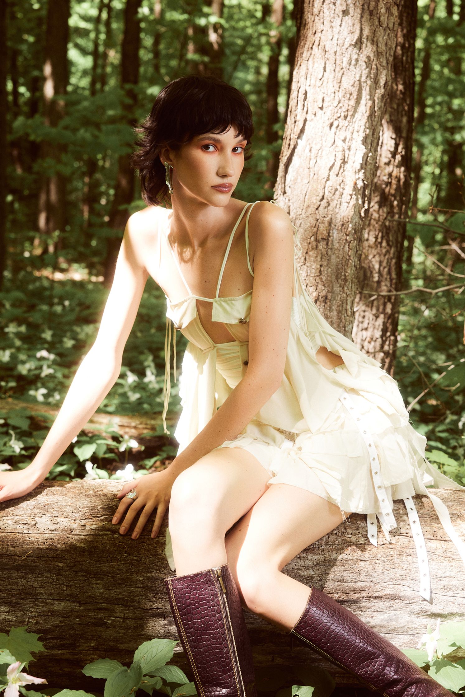 a woman in a white dress sitting on a log in the woods