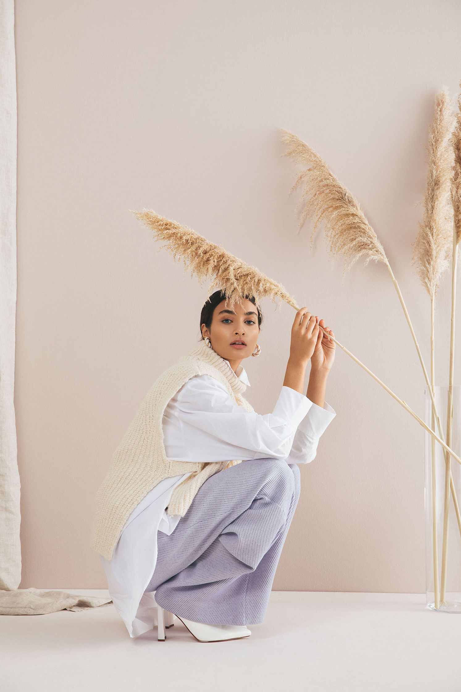 a woman crouching down next to a tall stalk of grass