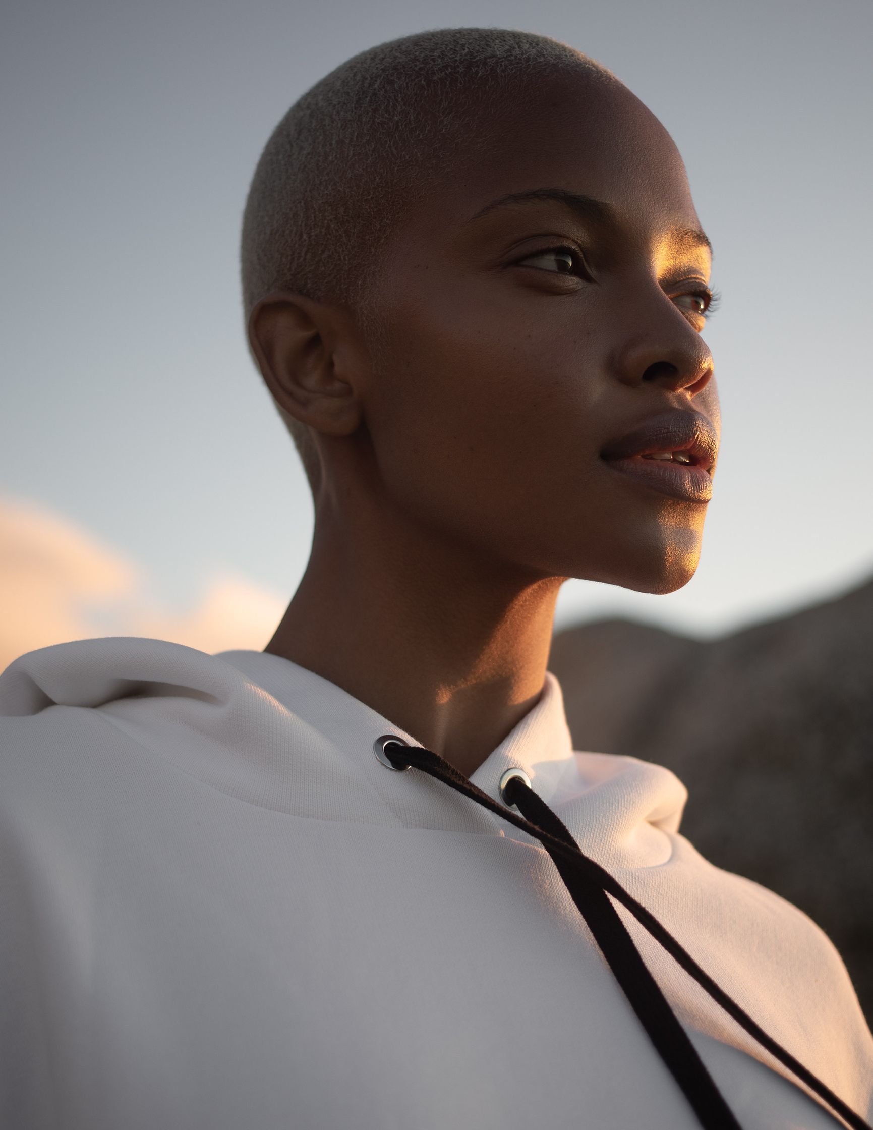 a black woman with a shaved head in a white hoodie