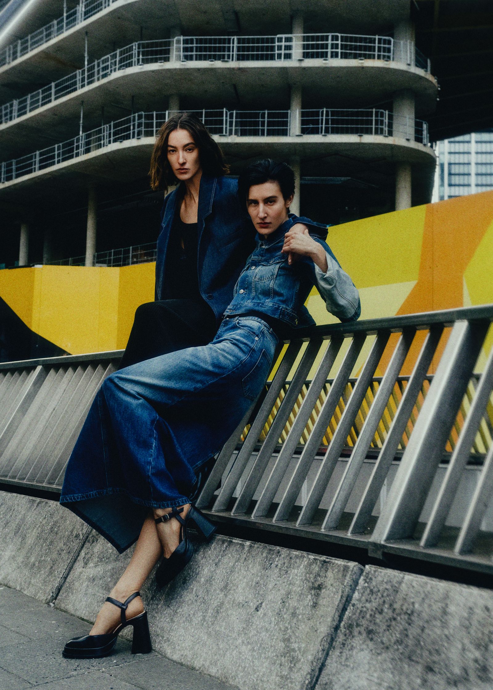 two women posing on a railing in front of a building
