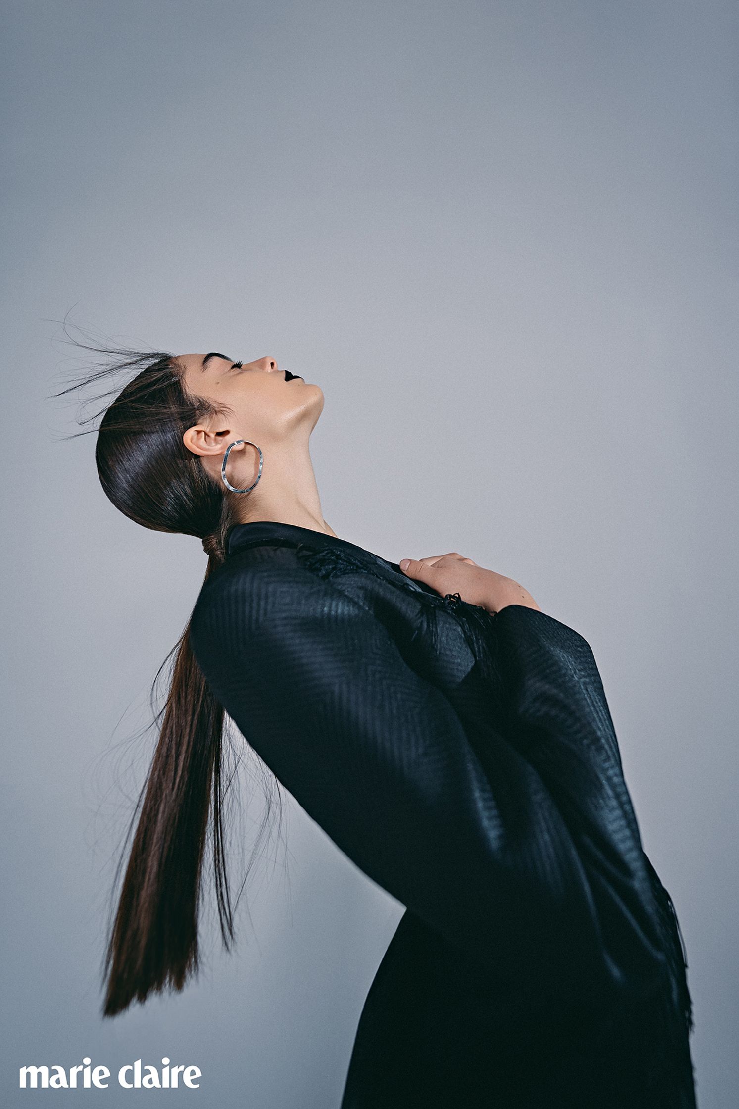 a woman in a black suit is posing with her hair in the air