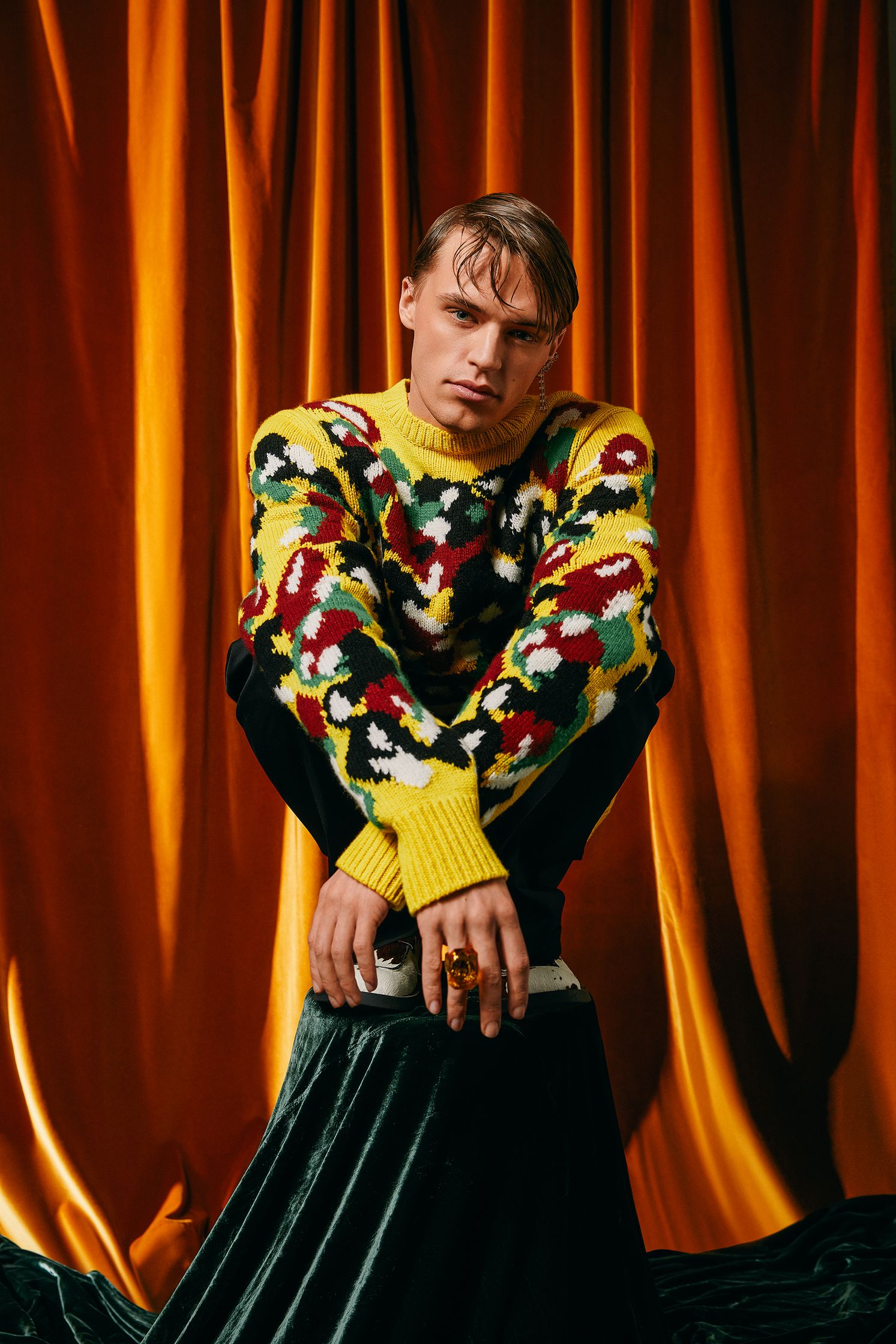 a man in a colorful sweater posing on top of a curtain
