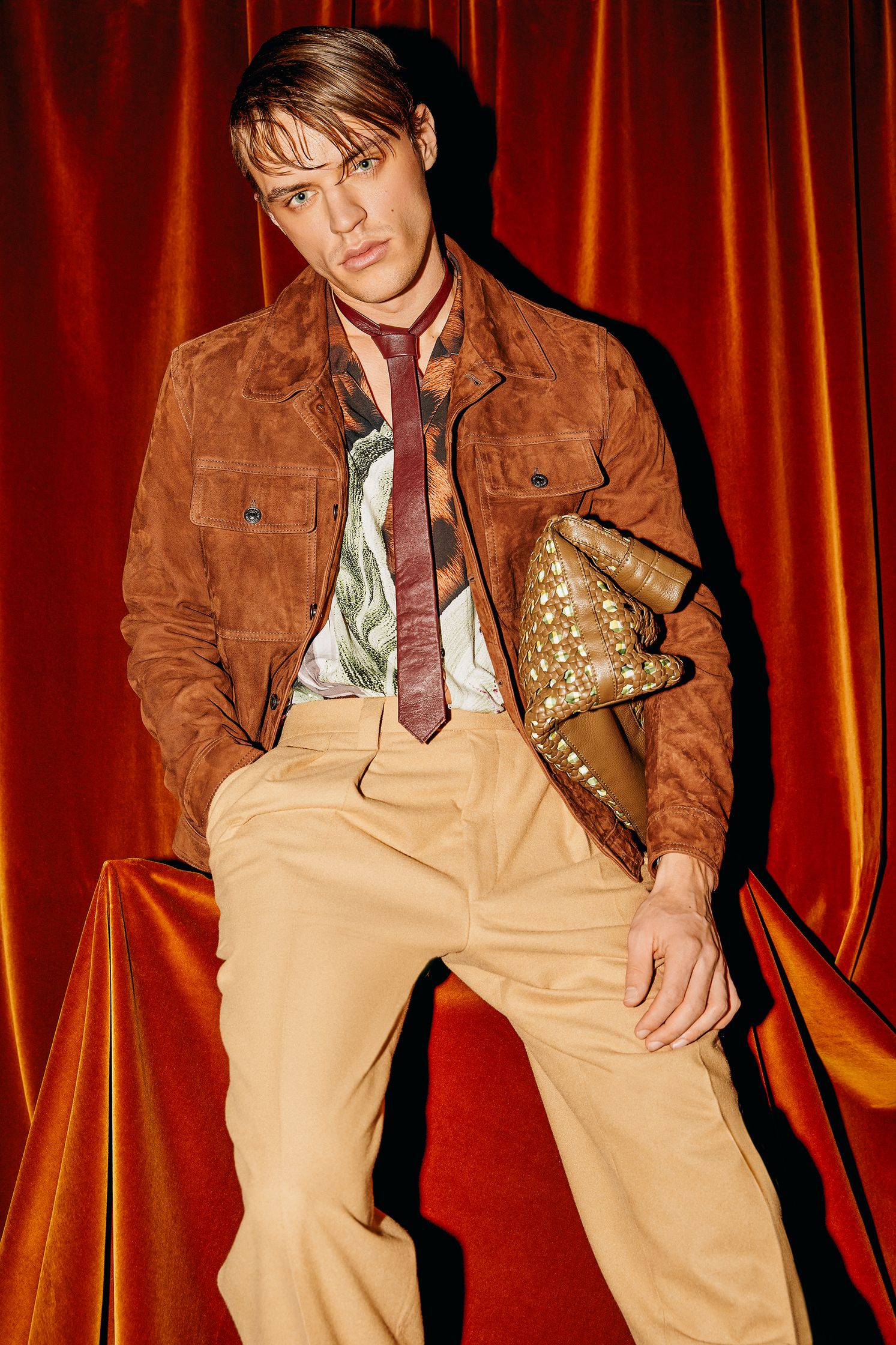 a man in a tan jacket sitting on a red curtain