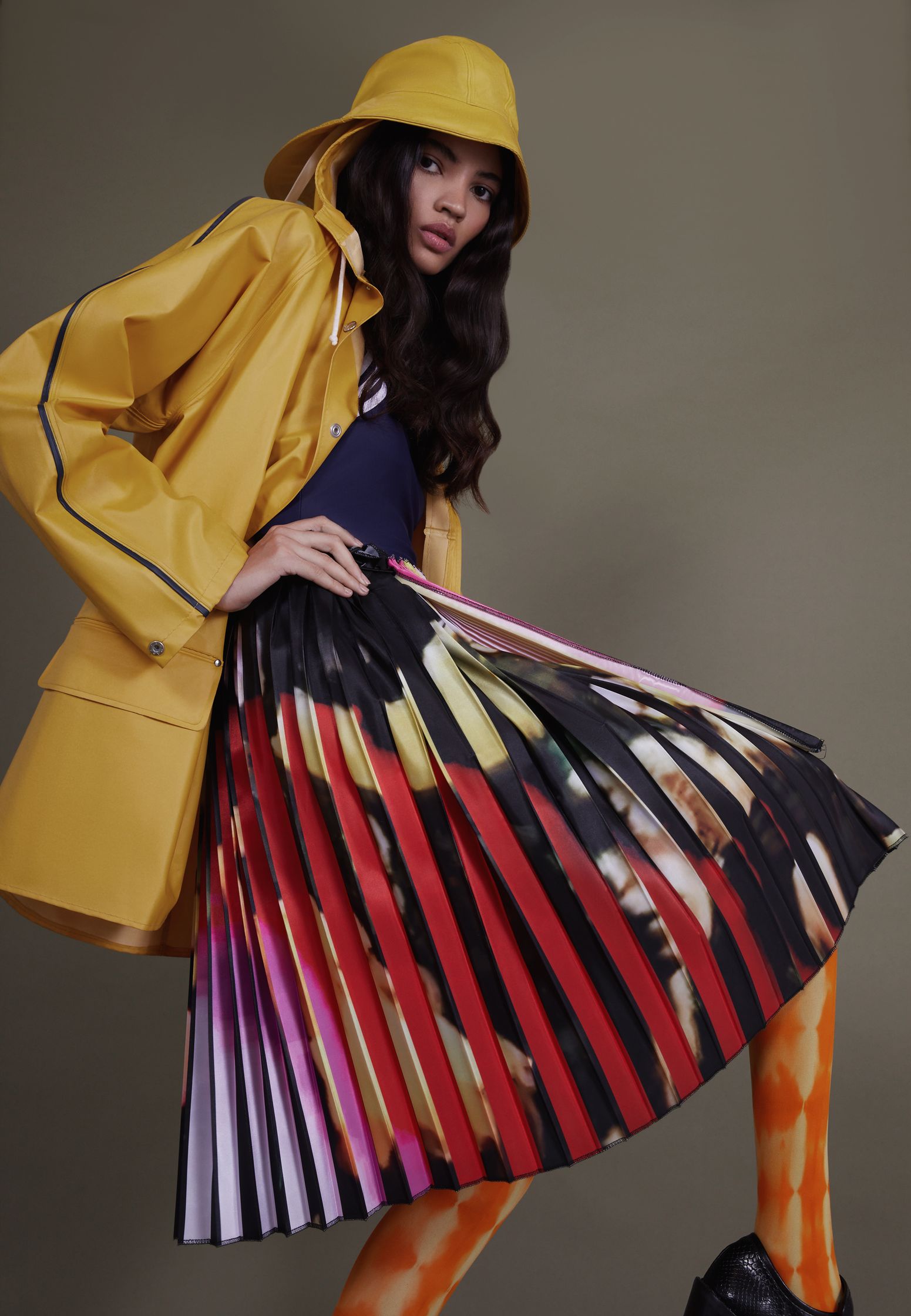 a woman in a yellow raincoat and pleated skirt