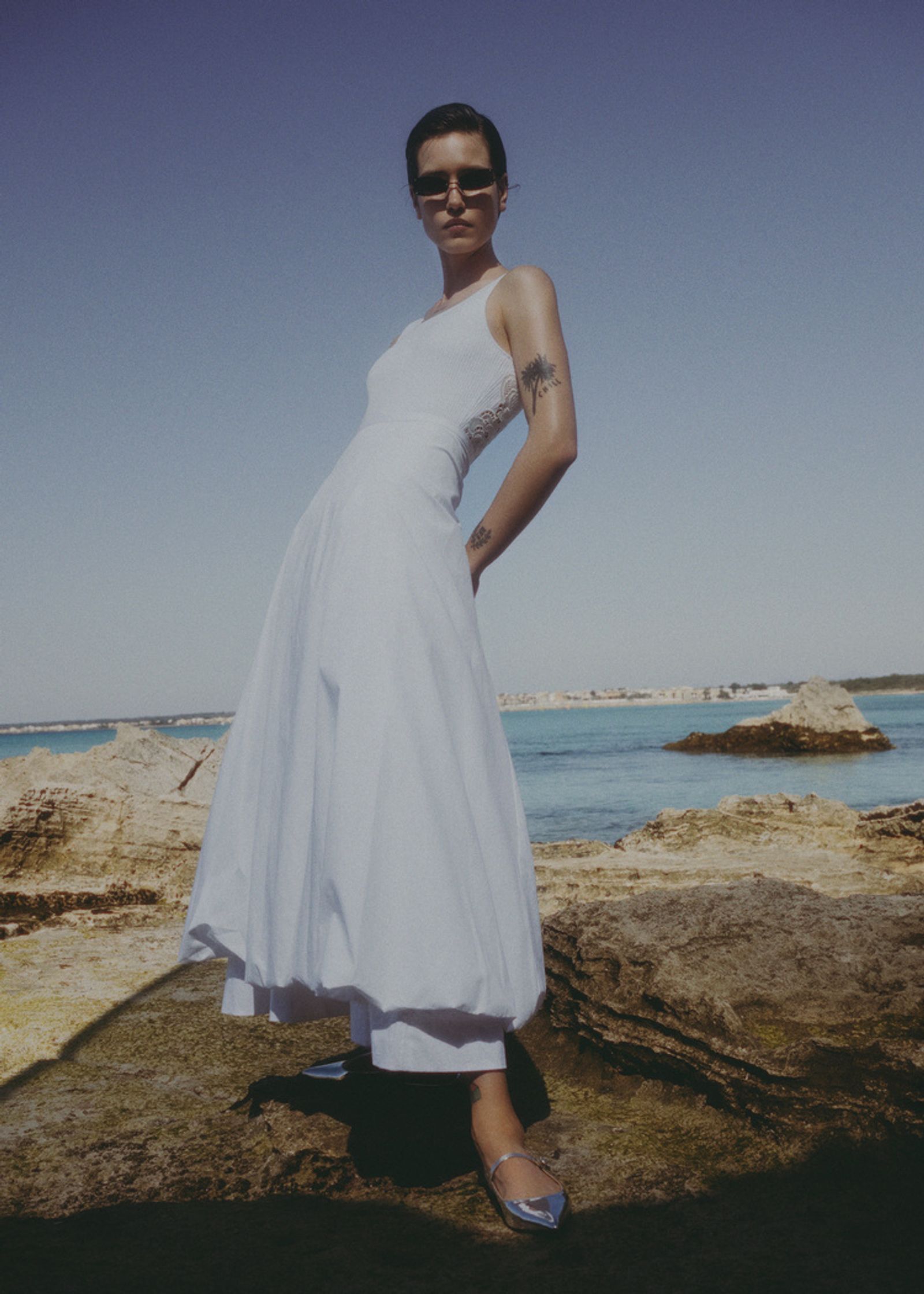 a woman in a white dress standing on rocks near the ocean
