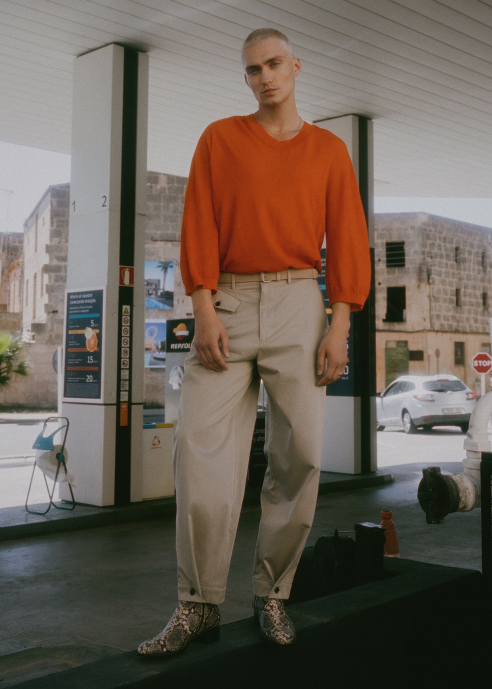 a man in an orange sweater standing in front of a gas station
