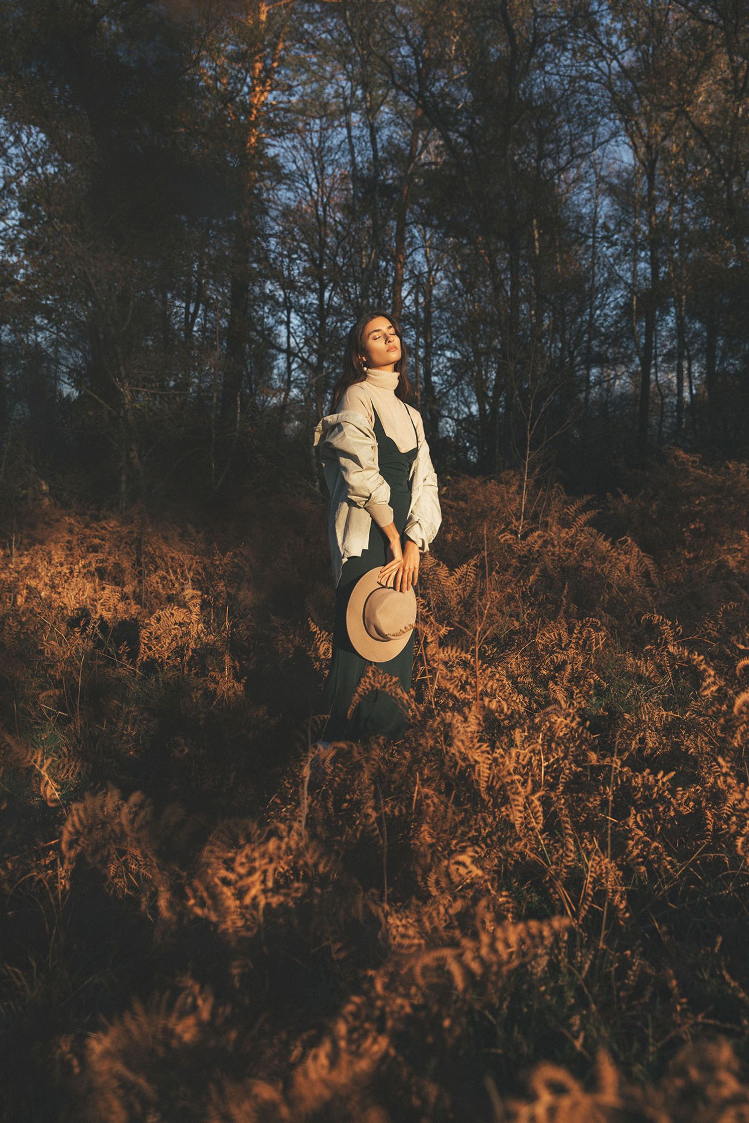 a woman standing in a forest with a hat