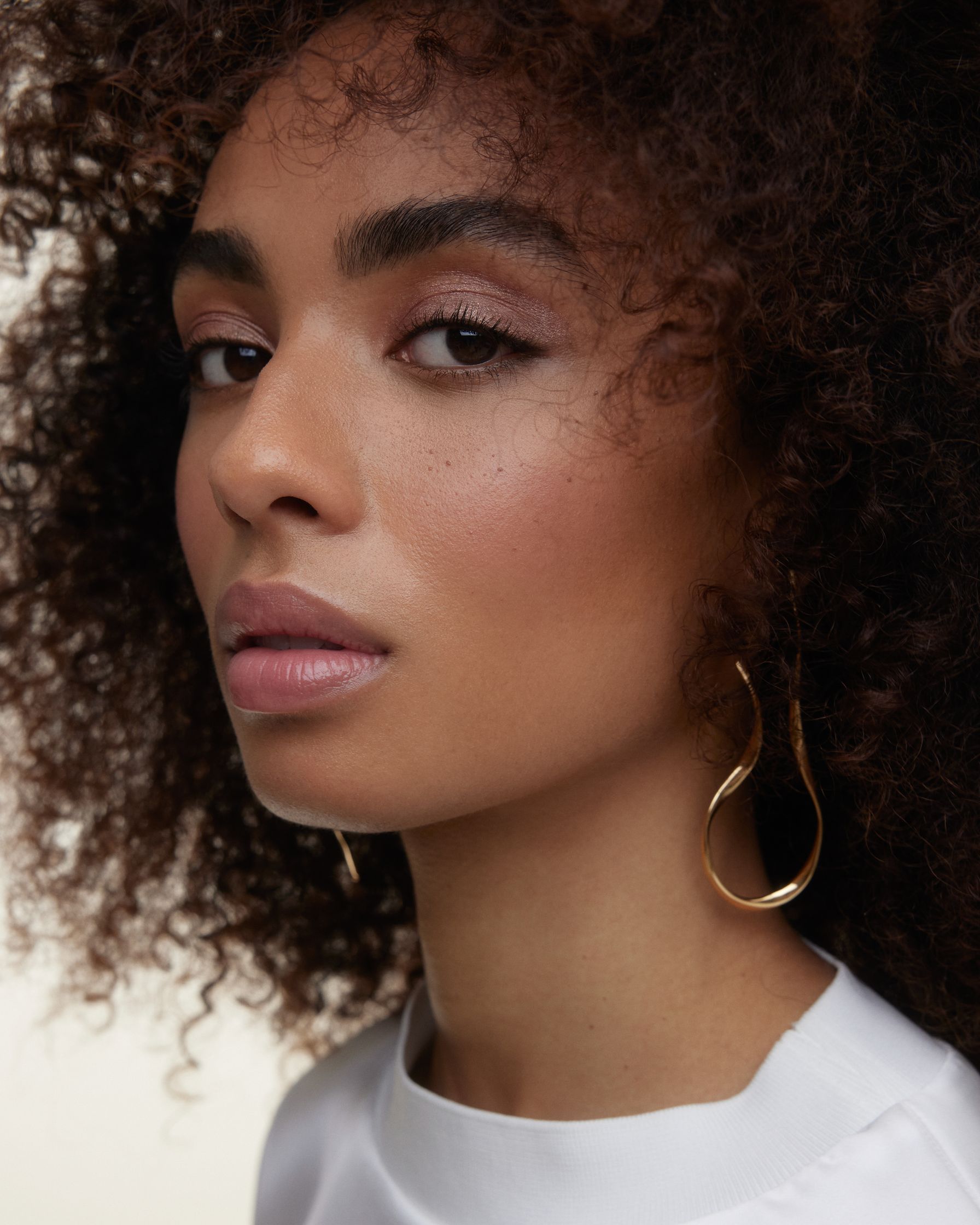 a woman with curly hair and gold earrings