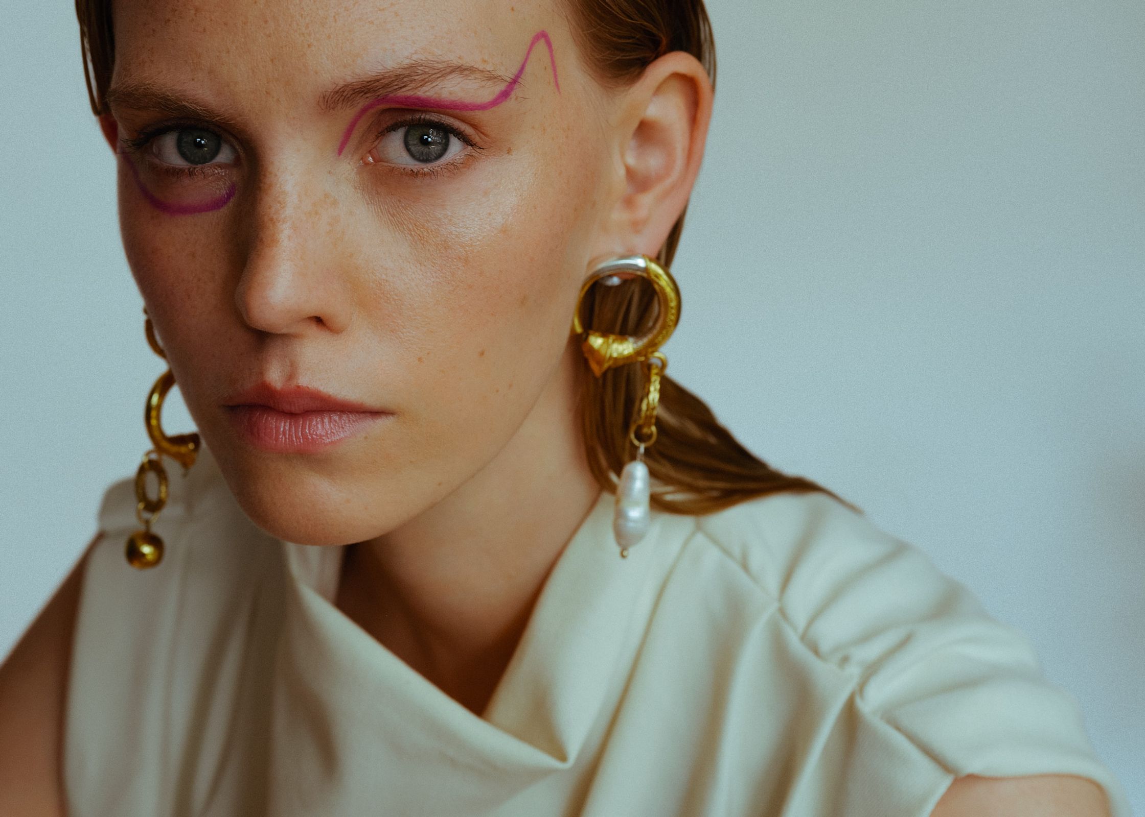 a woman with pink eye makeup and gold earrings