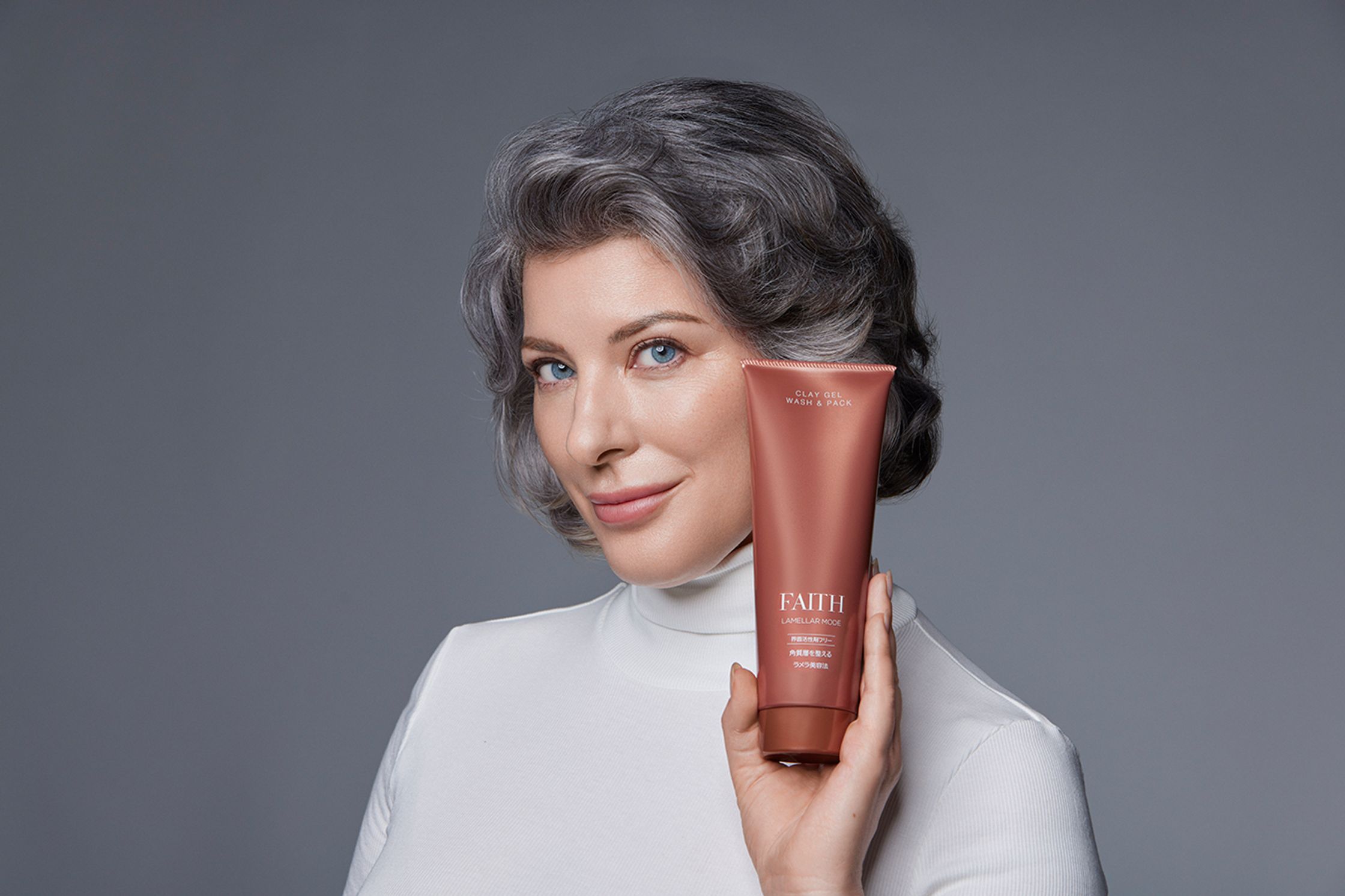 a woman with gray hair holding a tube of cream