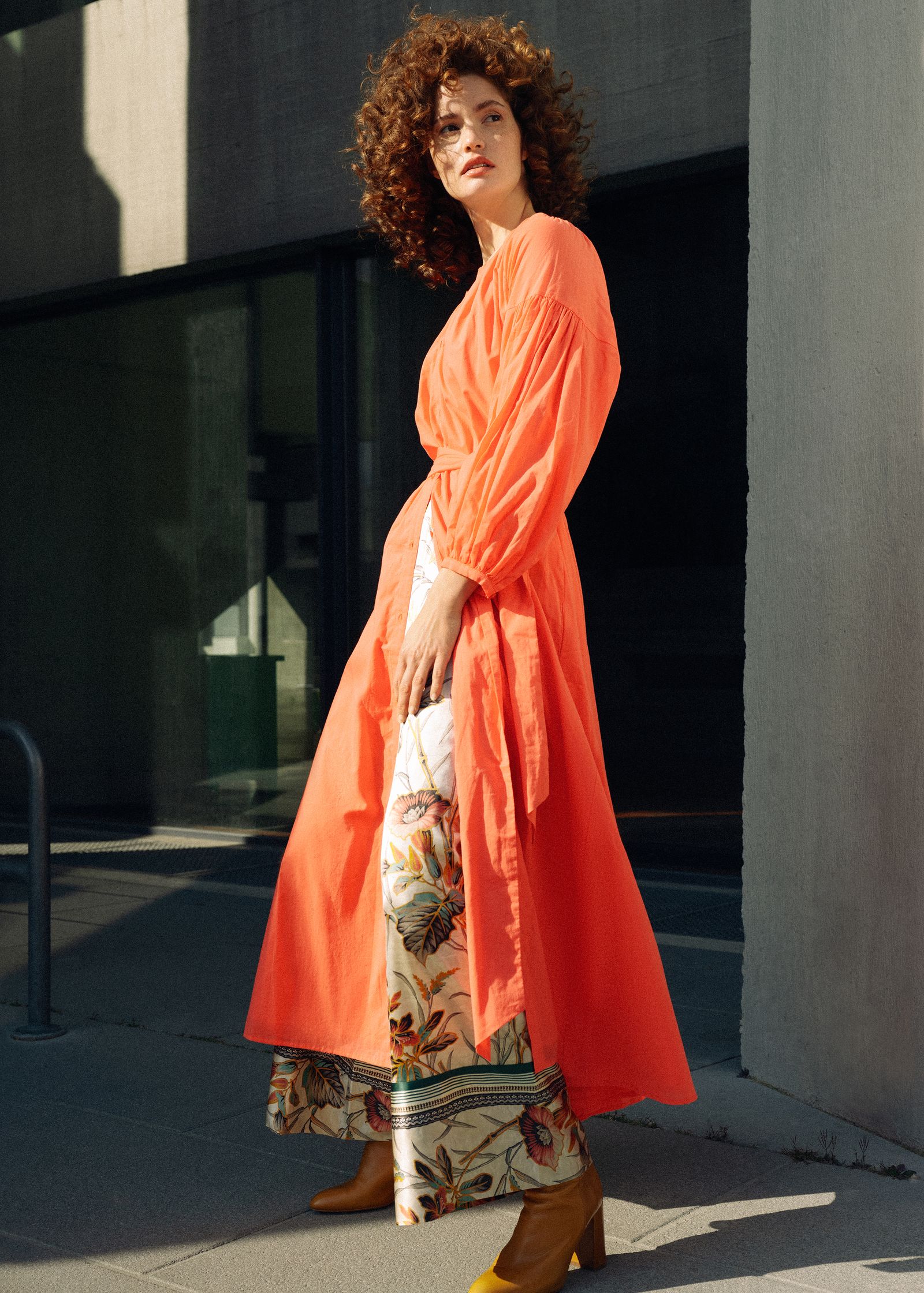 a woman in an orange dress is standing in front of a building