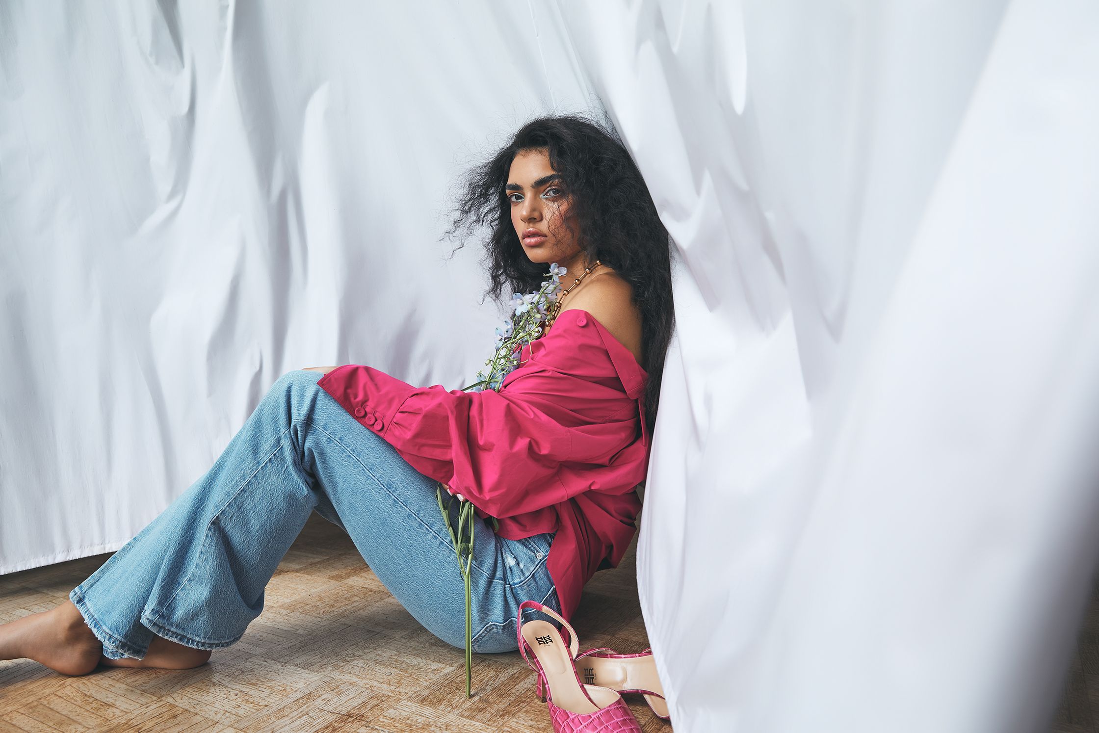 a woman sitting on the floor in a pink top and jeans