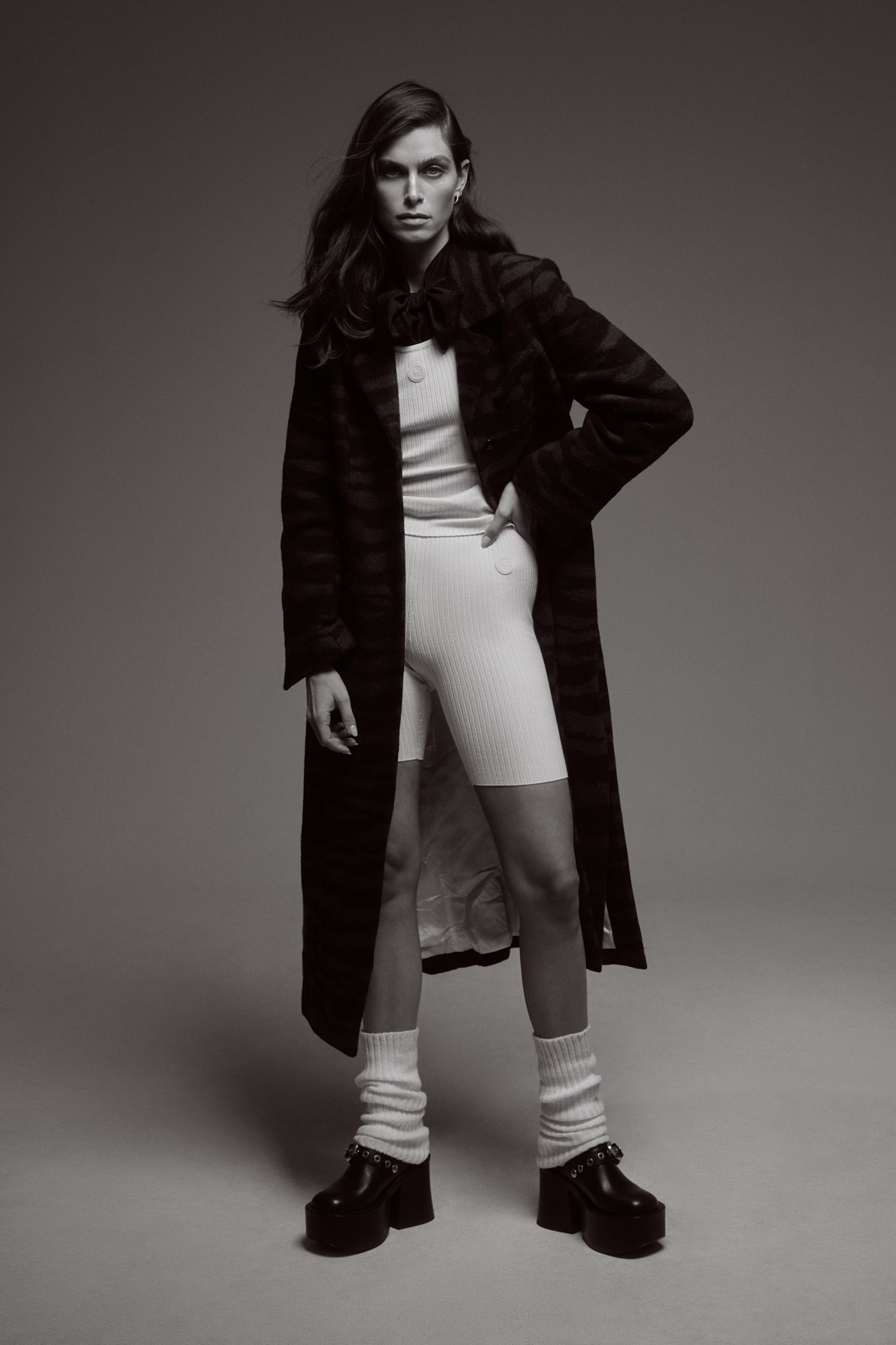 a black and white photo of a woman in a coat and shorts