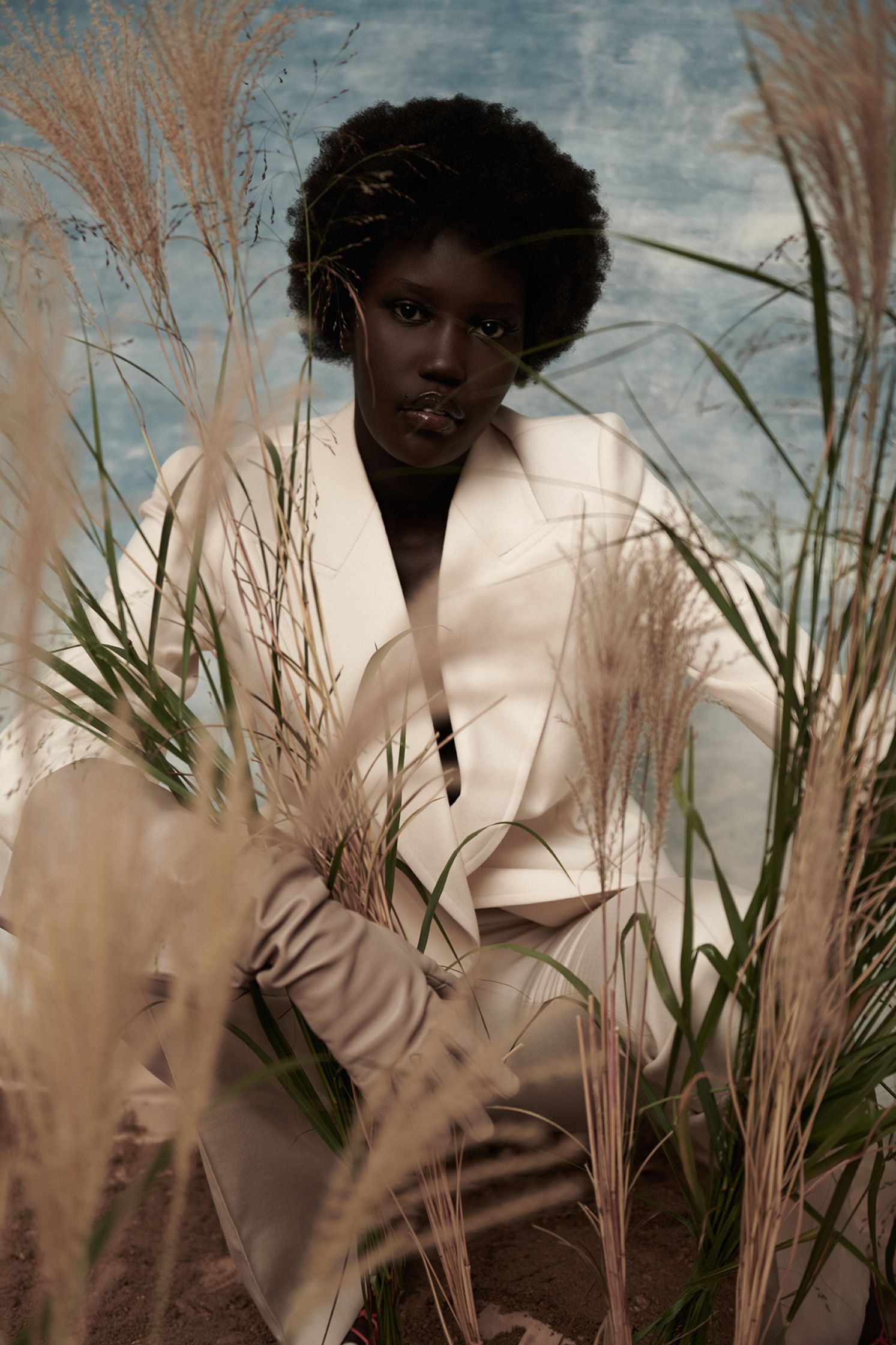 a woman in a white suit sitting in tall grass