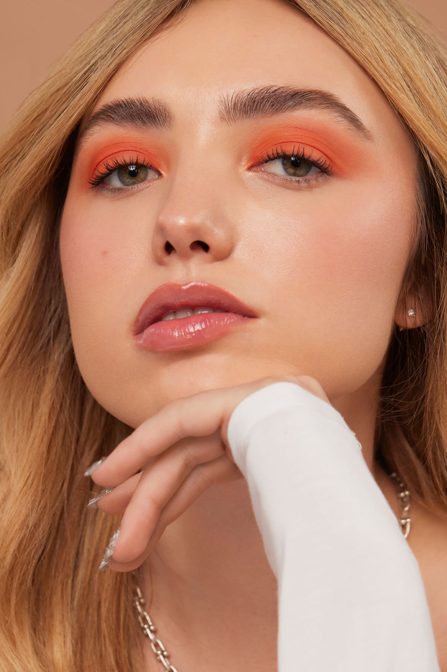 a woman wearing orange eyeshadow and a white necklace