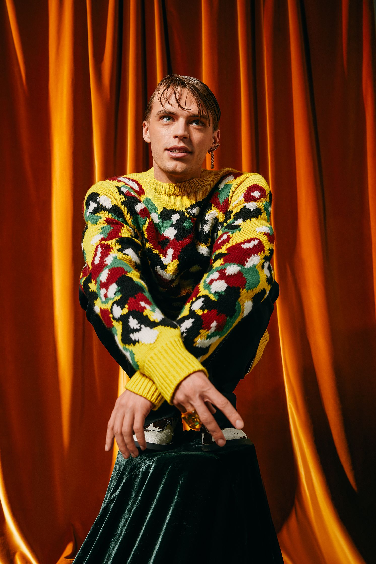 a man in a colorful sweater posing on top of a curtain