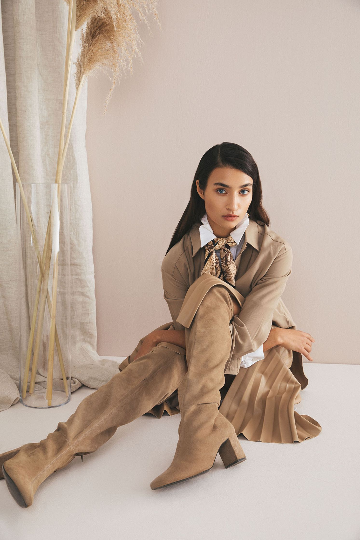 a woman is sitting on the floor in a beige coat and thigh high boots