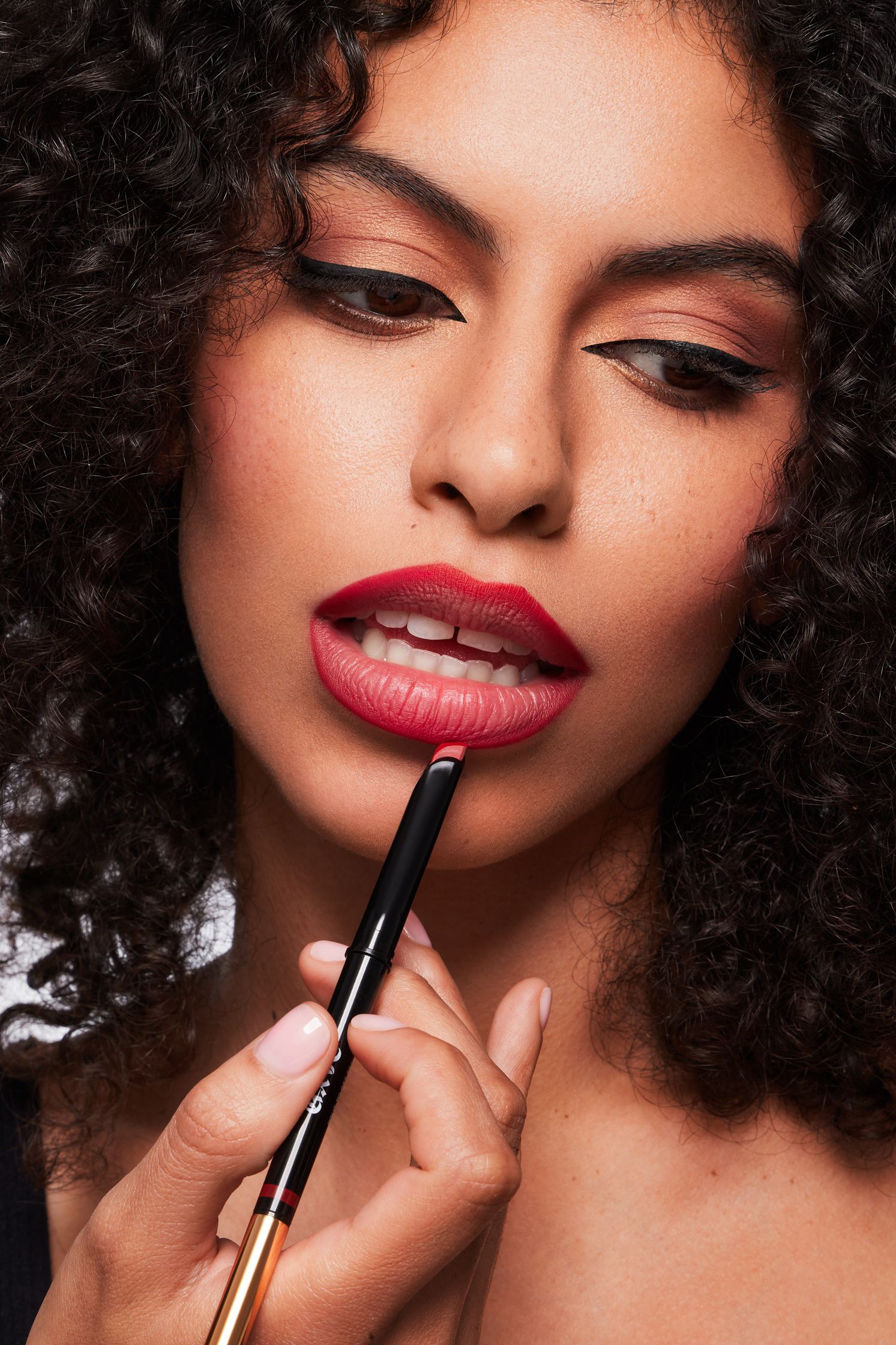 a woman with curly hair is applying lipstick with a brush