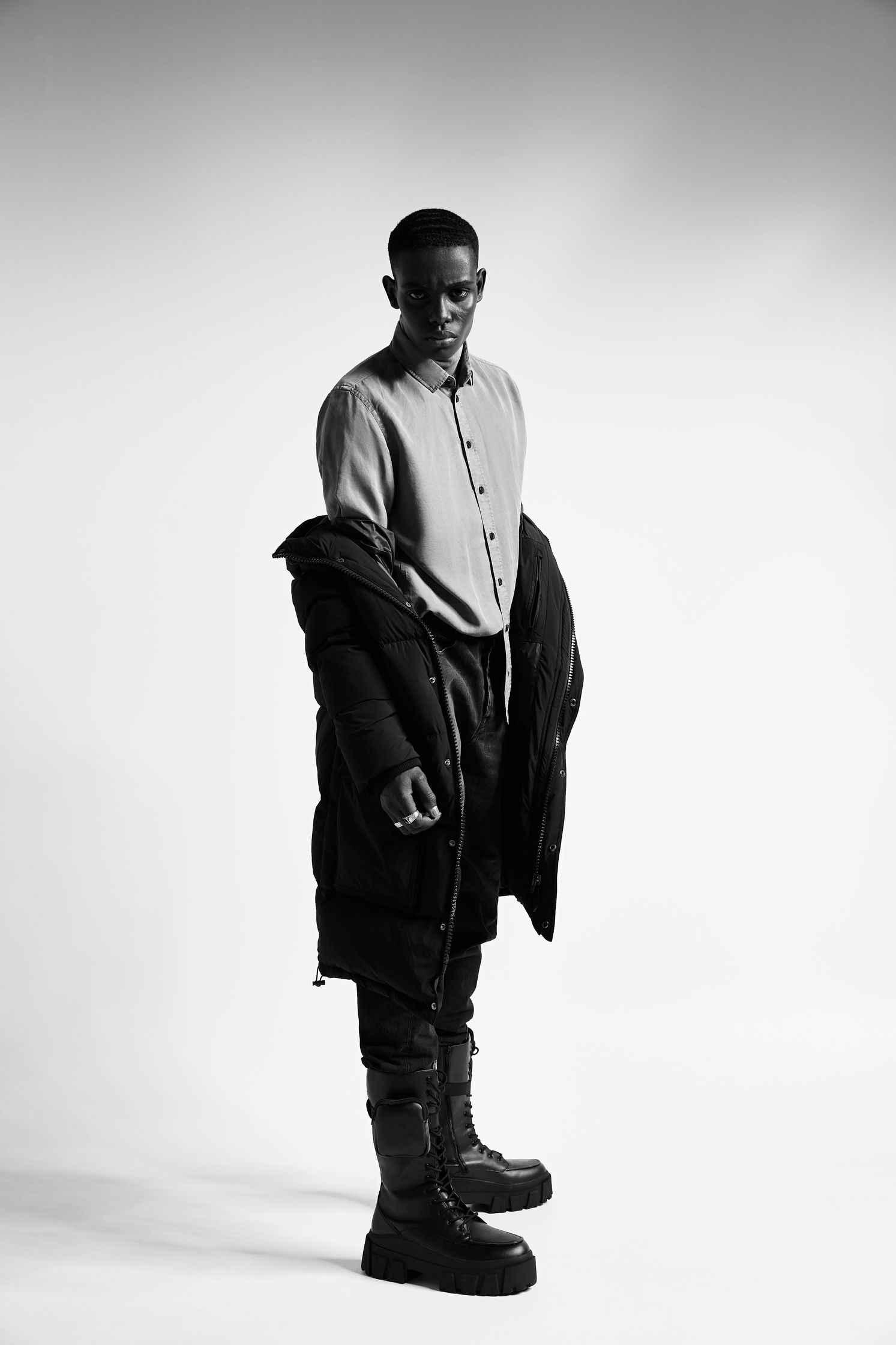 a black and white photo of a man in a jacket and boots